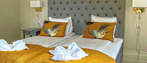 Una cama doble con cabecera gris capitonada, dos almohadas a juego, una mesita de noche con lámpara y una colcha amarilla estampada.