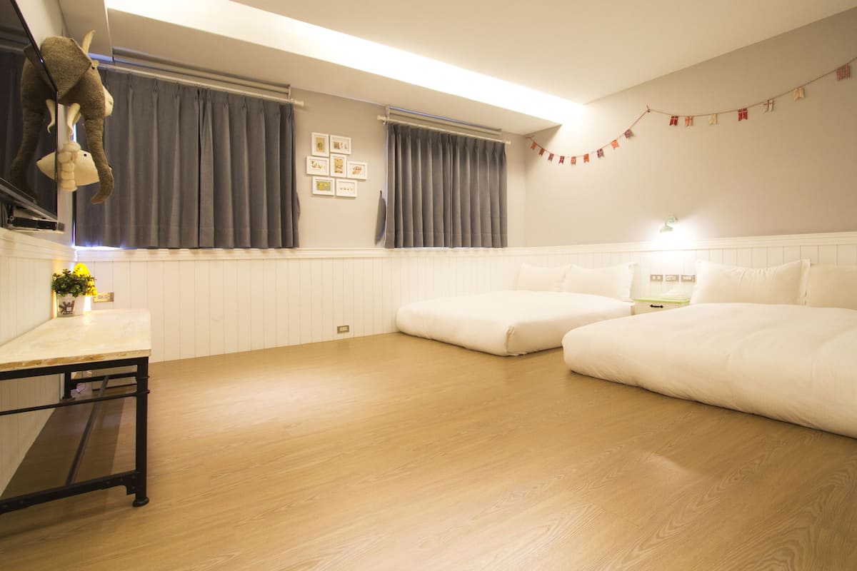 Ein Hotelzimmer mit Holzboden, einem Bett, einem Nachttisch, einer Lampe und einem Fenster mit Vorhängen.