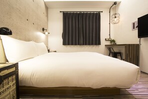 A hotel room with a large bed, a desk, a chair, a lamp, and a TV mounted on the wall. - RA Guesthouse (Hualien City)