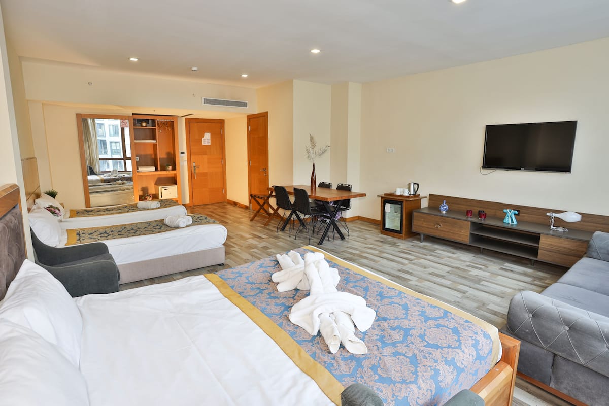 A hotel room with a bed, a sofa, a desk with a chair, a television, and a bathroom visible through an open door.