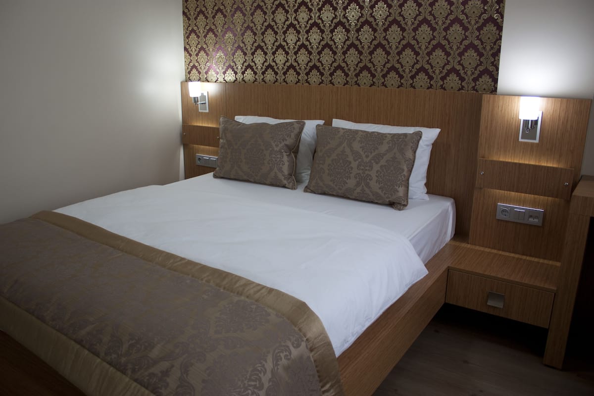 A hotel room with a wooden headboard, two bedside tables with lamps, a bed with white linens, and patterned throw pillows.