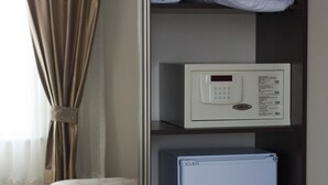 Una habitación de hotel con cama, un refrigerador blanco pequeño, un panel de control y mantas dobladas cuidadosamente en un estante.
