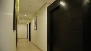 Een gang met een donkerhouten deur, een lijst met een afbeelding aan de muur, en een betegelde vloer.