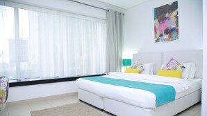 Een slaapkamer met een bed, een raam met gordijnen, een schilderij aan de muur en een lamp.