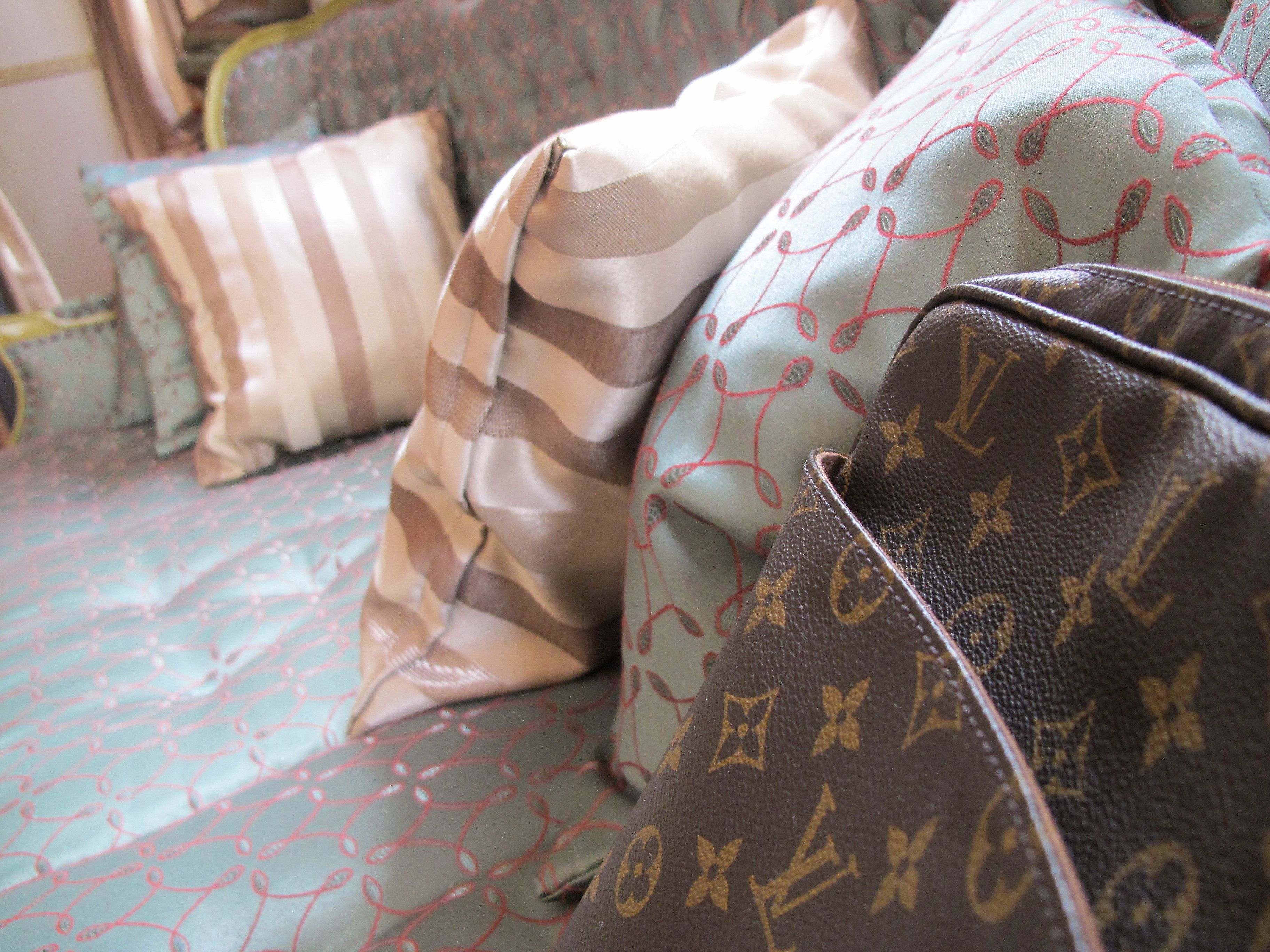 A bed with patterned bedding and pillows, including a striped pillow and a pillow with a monogram design.
