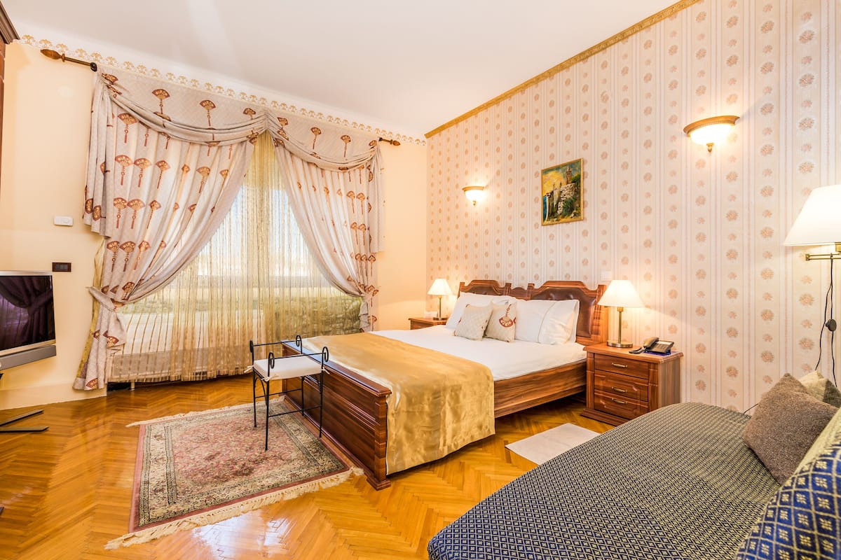 Un dormitorio con una cama grande, mesitas de noche, una silla, una alfombra y un cuadro en la pared.