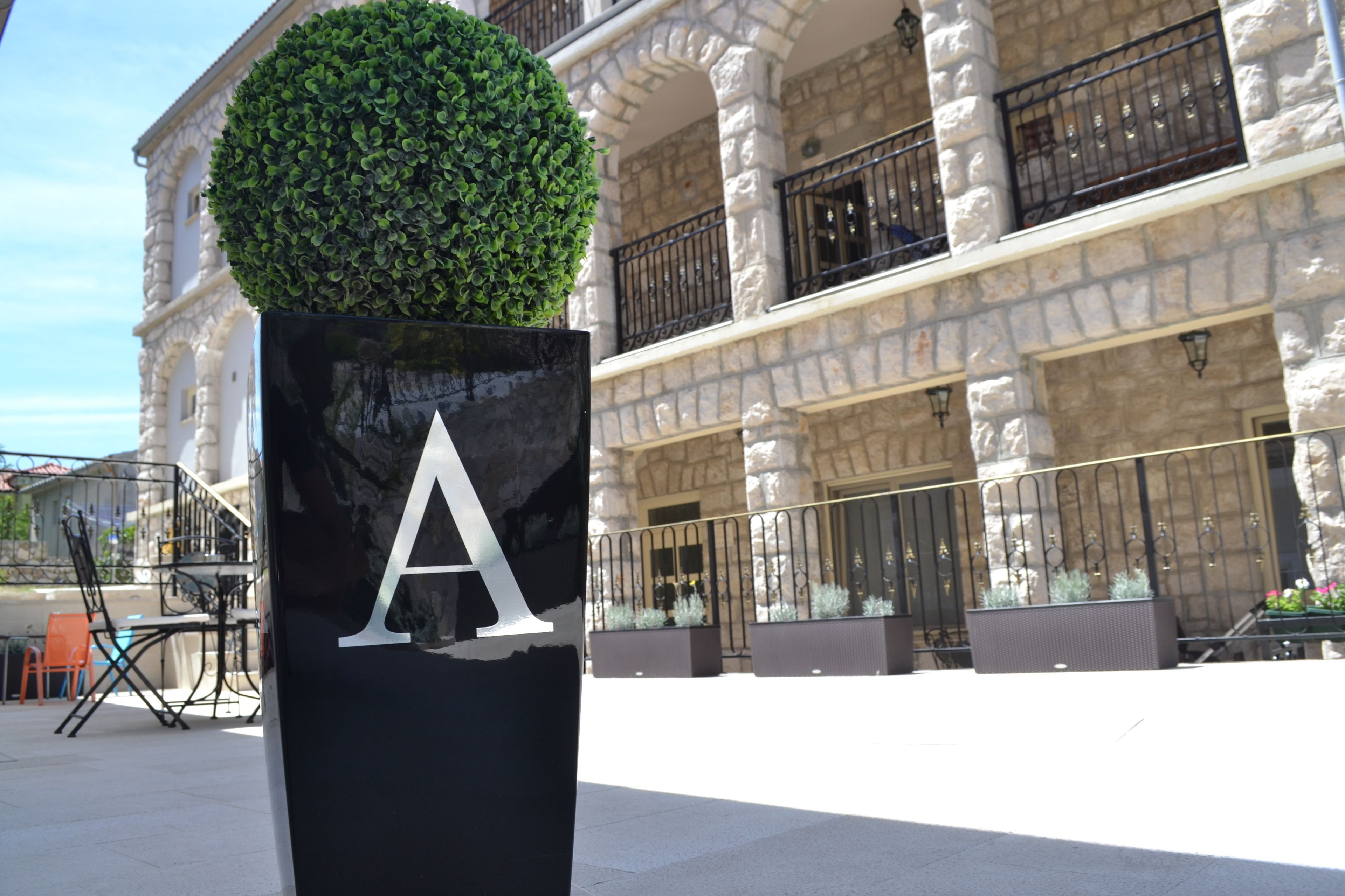 A building with a stone facade, black railings, and a large planter with a spherical topiary.