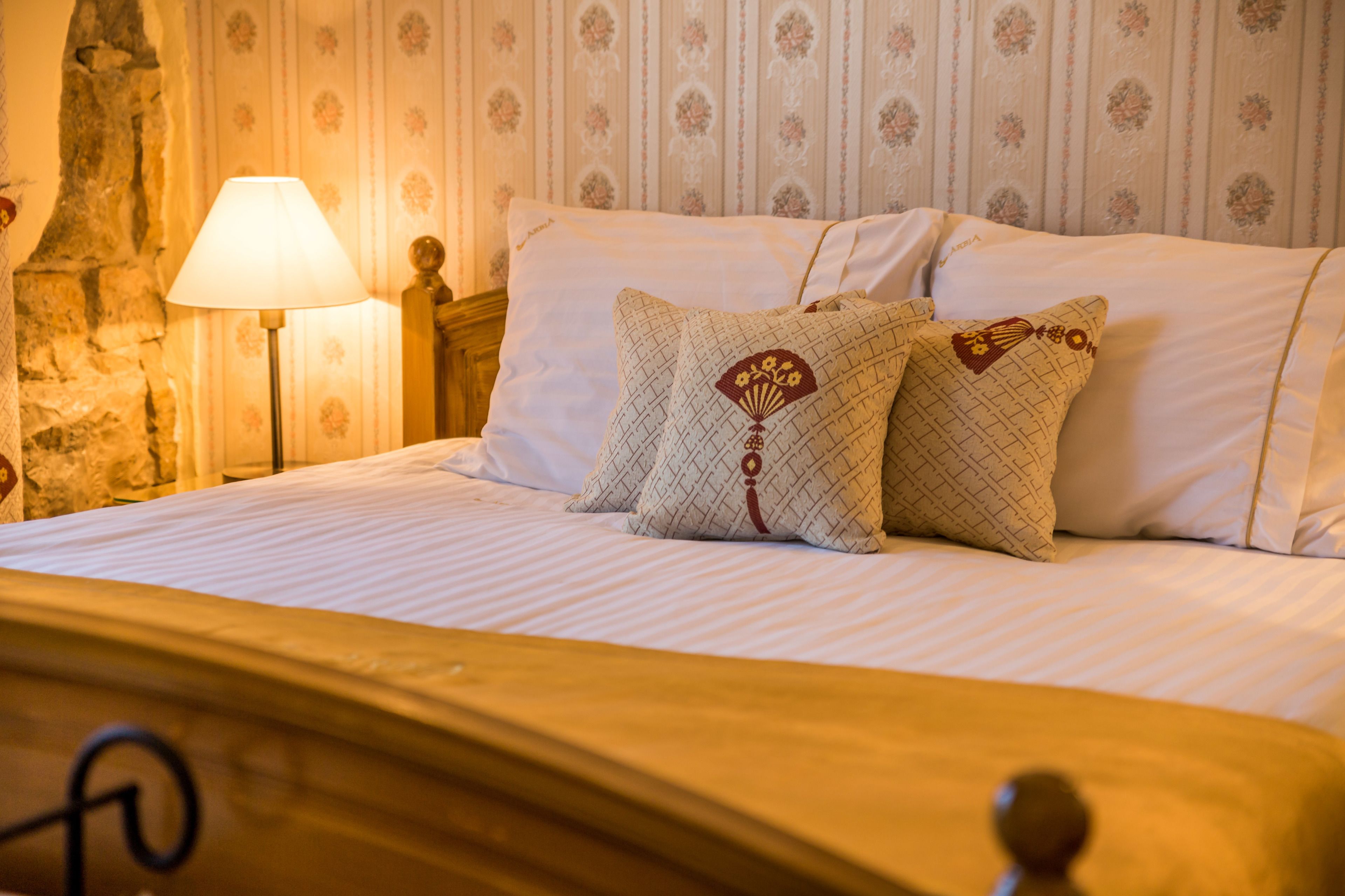 Una cama bien hecha con almohadas estampadas, un cabecero de madera y una lámpara en una mesita de noche.