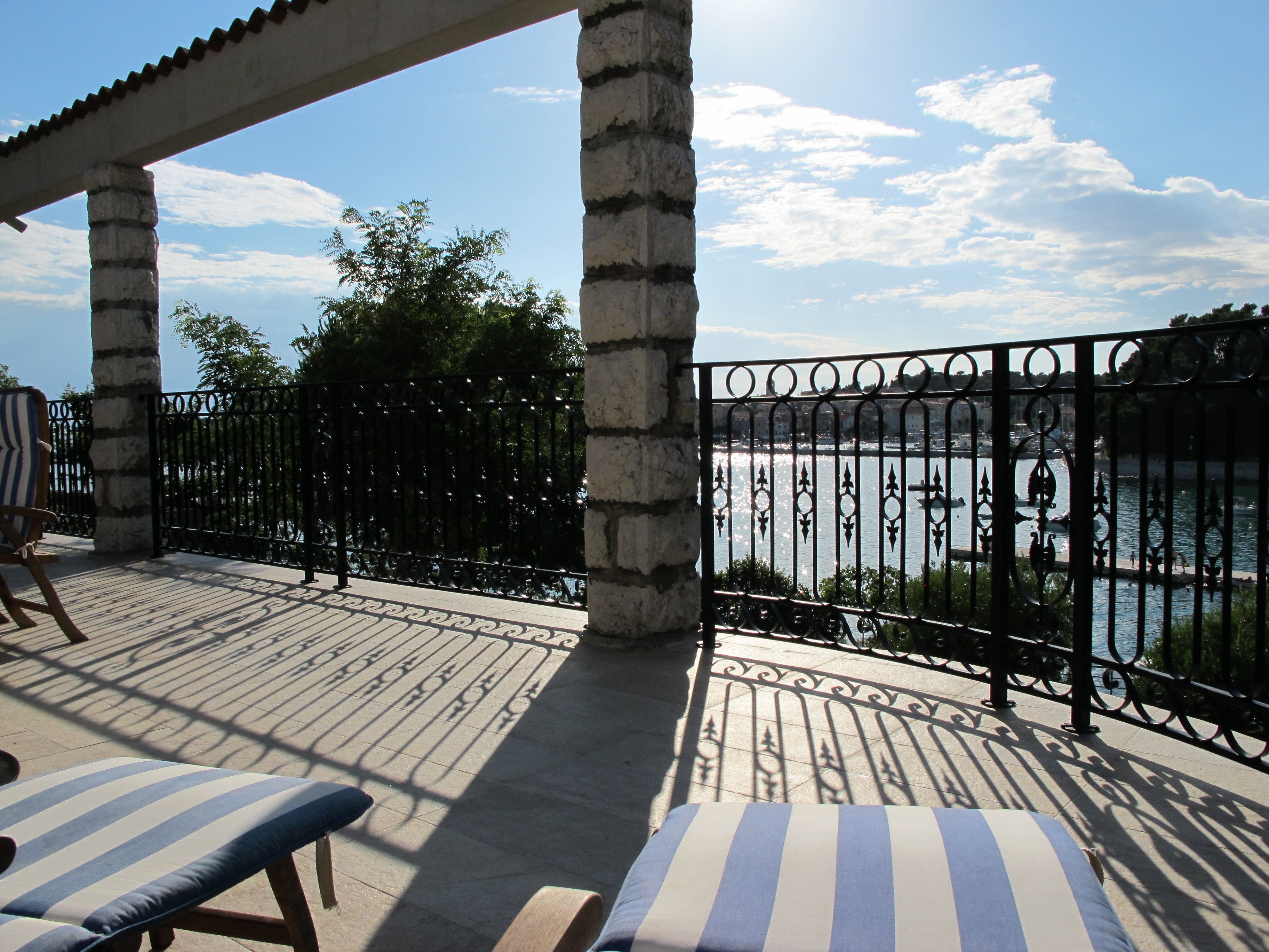 A terrace with a view of a body of water, stone pillars, and a metal railing.