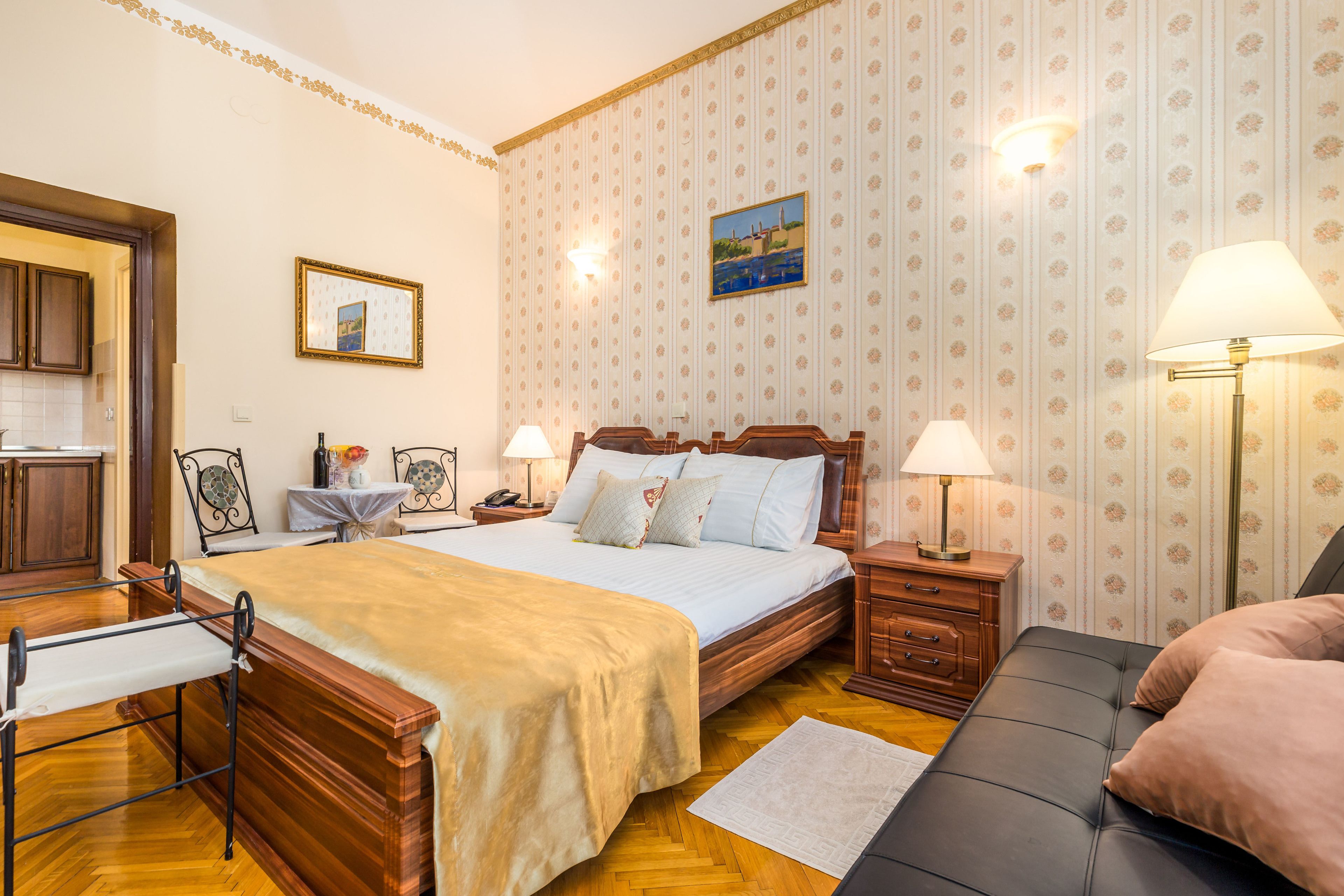 Un dormitorio ordenado con una cama de madera, mesitas de noche con lámparas, una pequeña mesa con un florero y una silla.