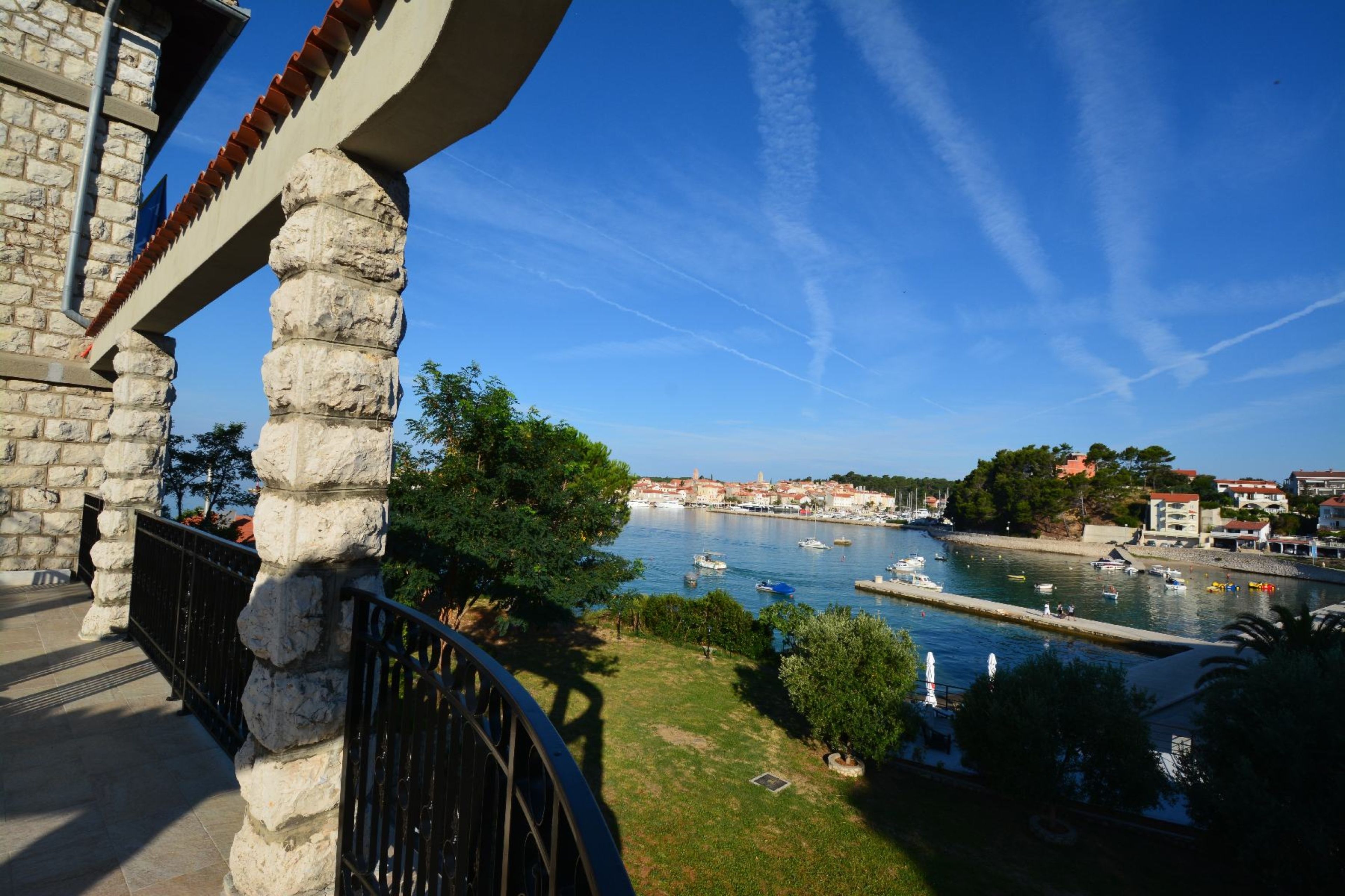 A stone building with a balcony overlooking a harbor with boats and a clear blue sky.
