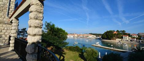 A stone building with a balcony overlooking a harbor with boats and a clear blue sky.