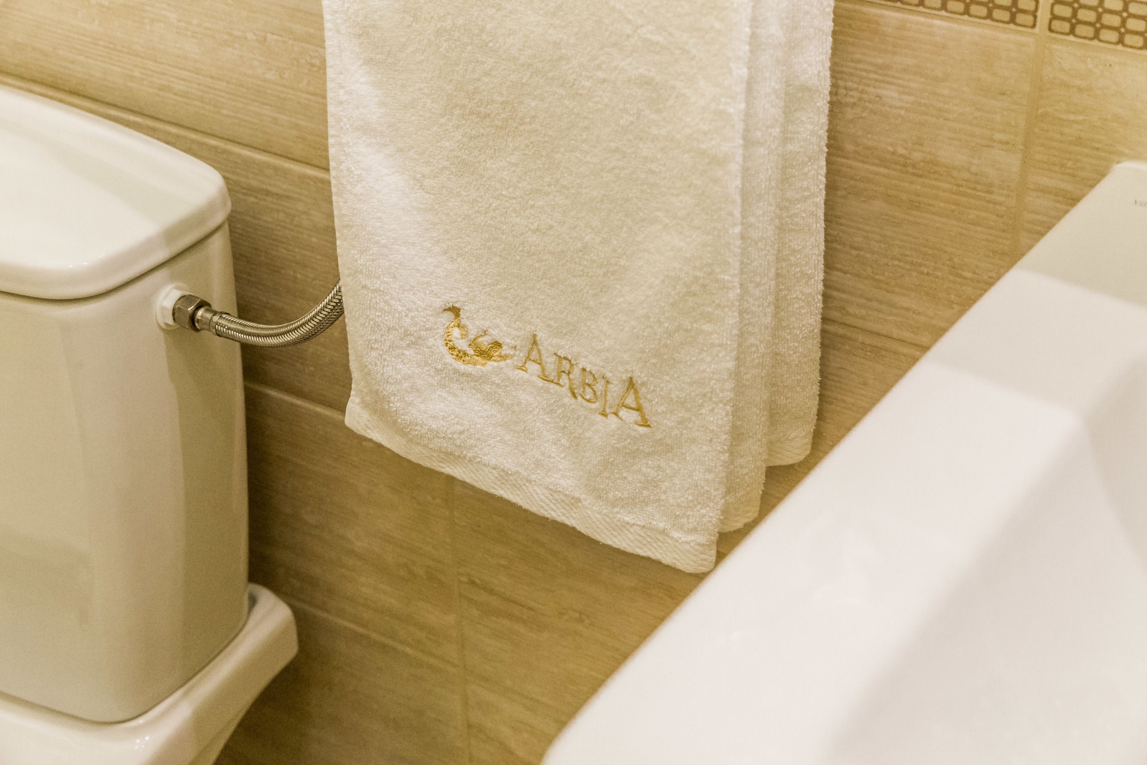 A bathroom with a white toilet, a white bathtub, and a towel hanging on the wall with the word "ARMENIA" embroidered on it.