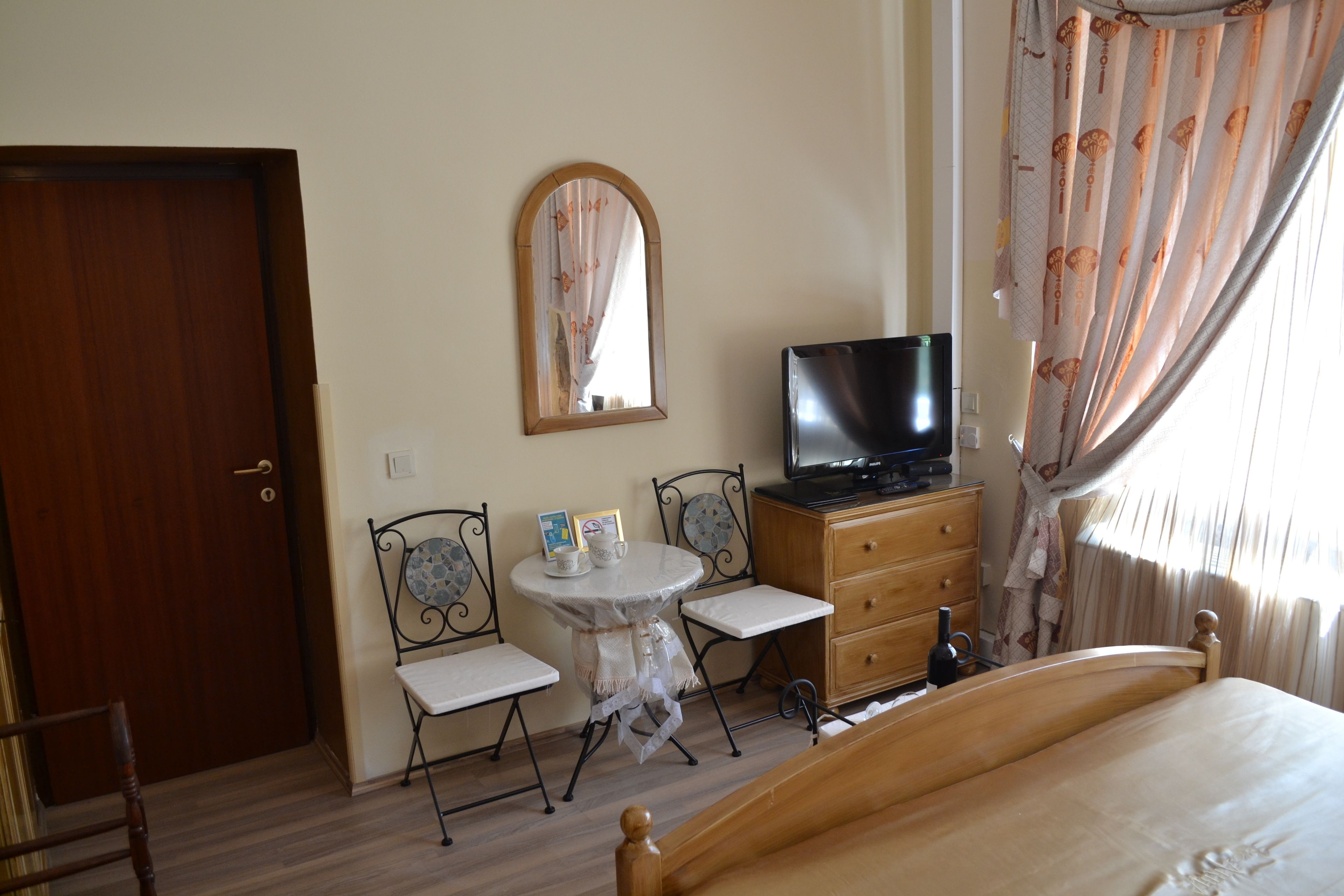 A bedroom with a wooden bed, a television on a wooden dresser, a small round table with chairs, and a mirror on the wall.
