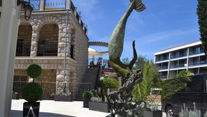 Un edificio de piedra con un balcón, una estatua de sirena y un coche aparcado cerca.