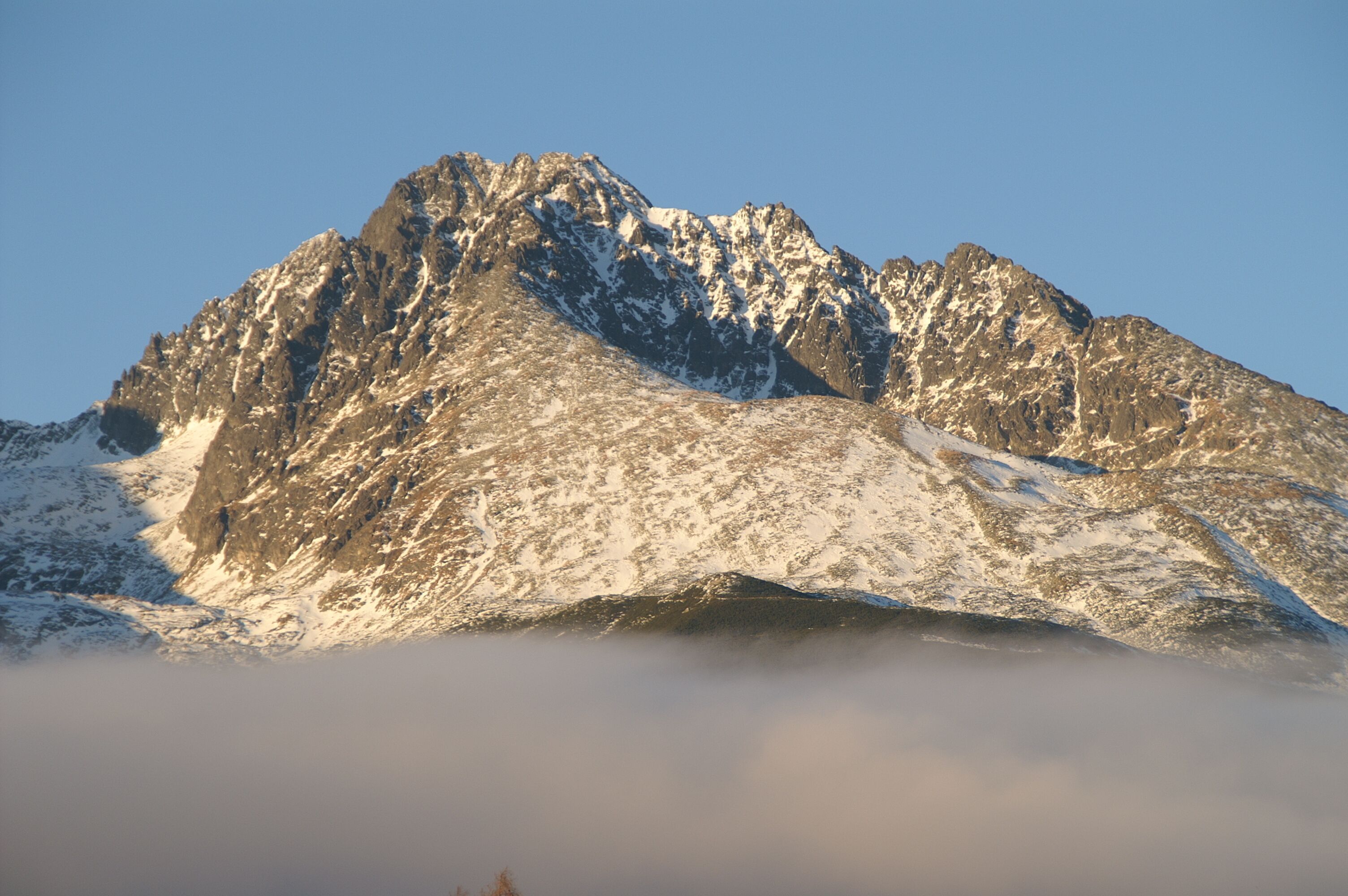 A mountain with snow-covered peaks and a clear sky.