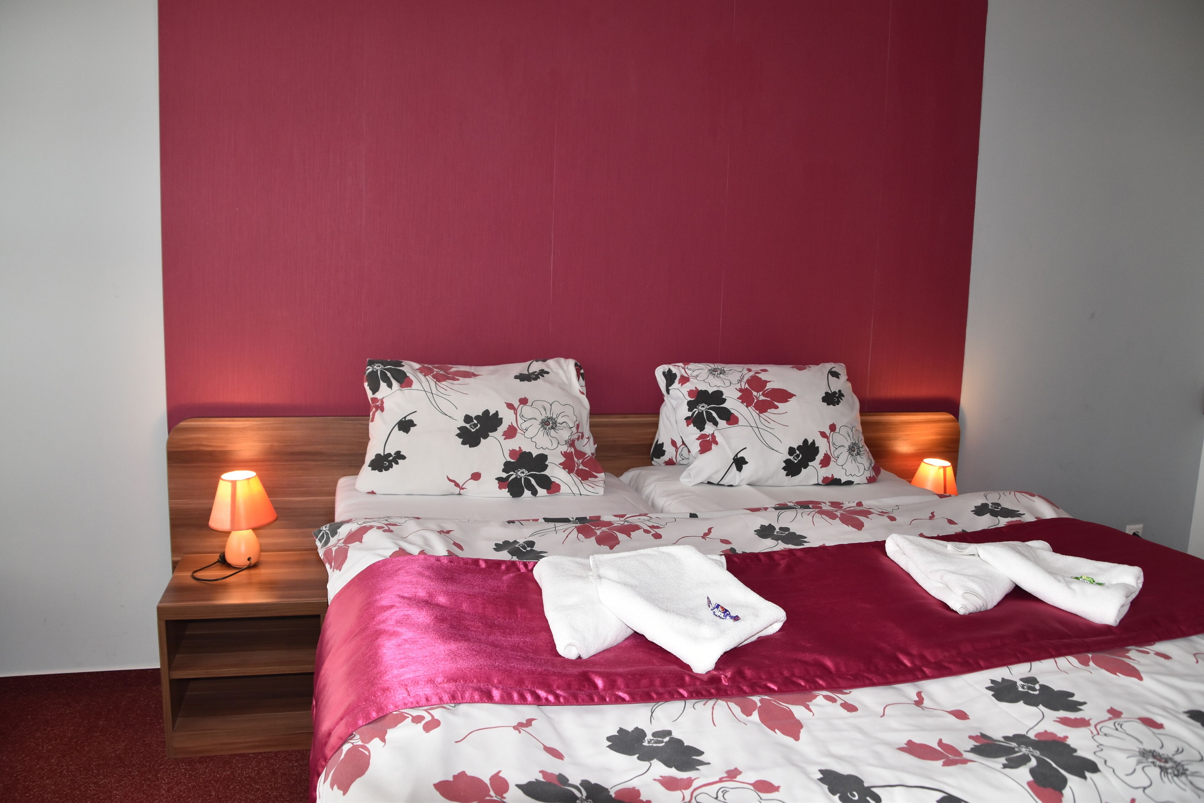 A neatly made bed with floral bedding, two pillows, and a red throw blanket. There are two bedside lamps on wooden nightstands.