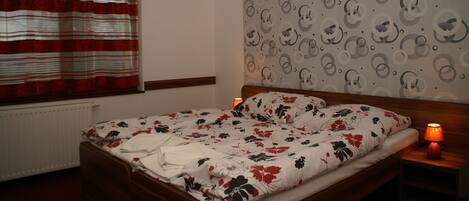 A bedroom with a bed, a window with curtains, a wall with a circular pattern, and a bedside lamp.