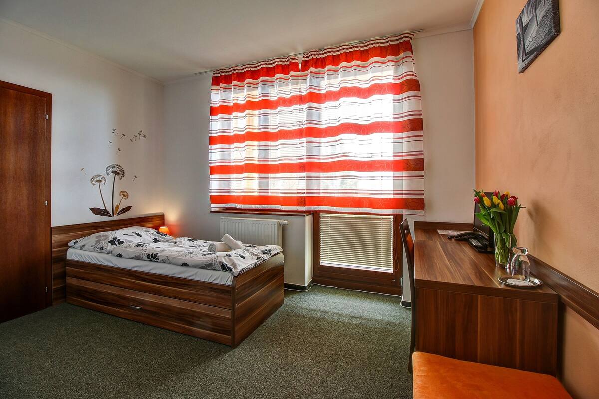 A bedroom with a wooden bed, a desk, and a window with striped curtains.