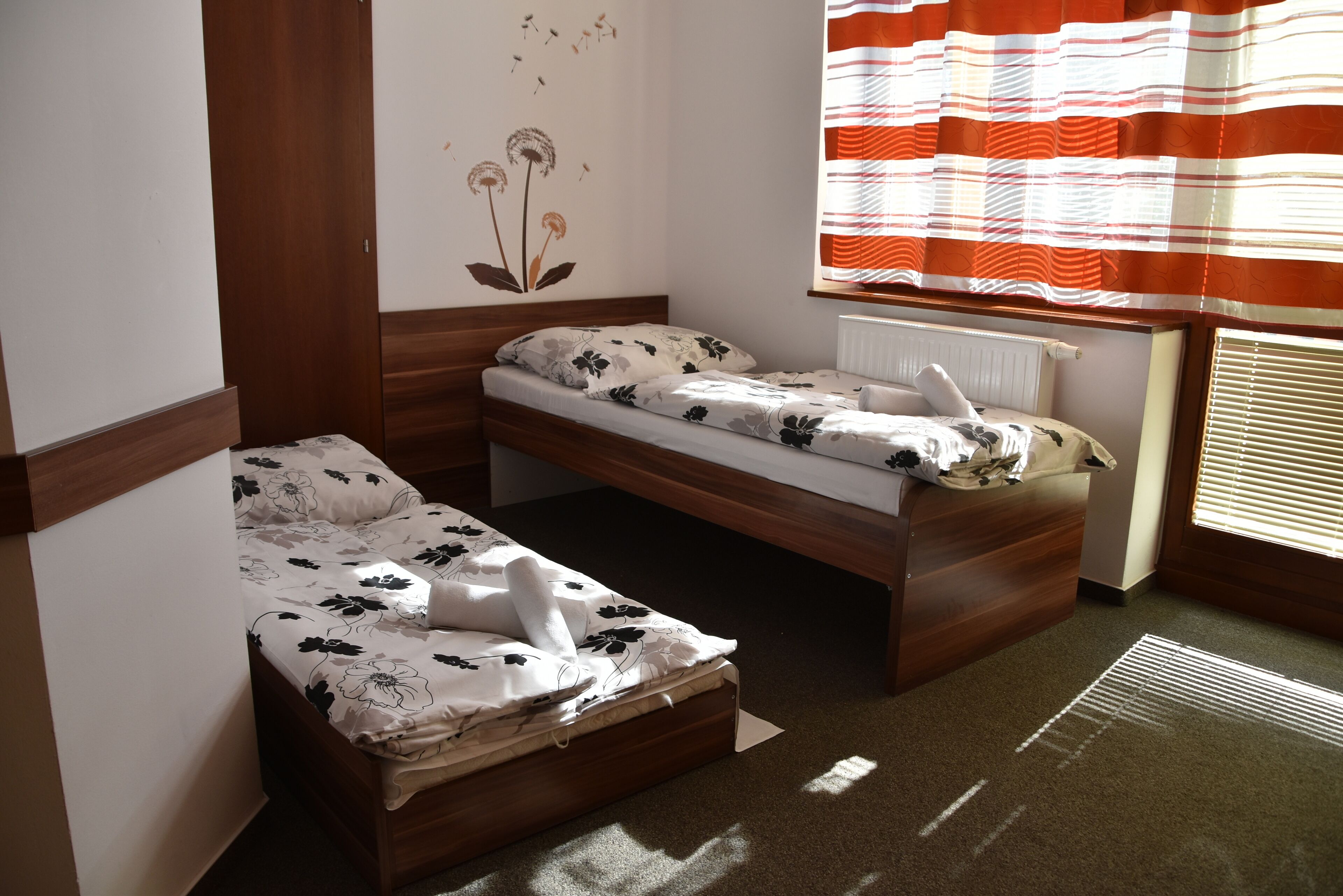 Une petite chambre avec un lit simple, une tête de lit en bois, un radiateur et une fenêtre ornée de rideaux à rayures.