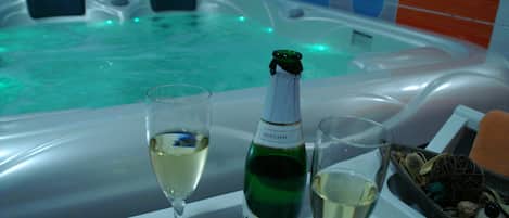 Un jacuzzi con una botella de champán y copas de vino blanco.