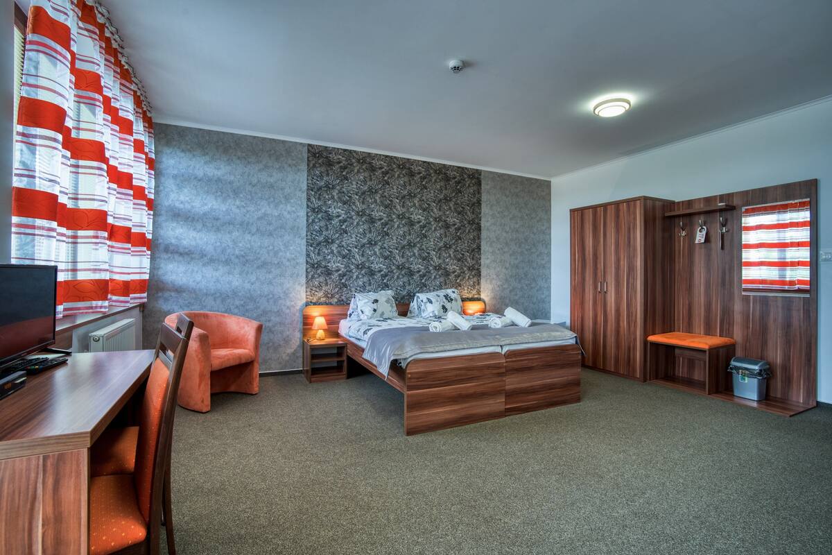 A modern bedroom with a large bed, a desk, a chair, and a wardrobe.