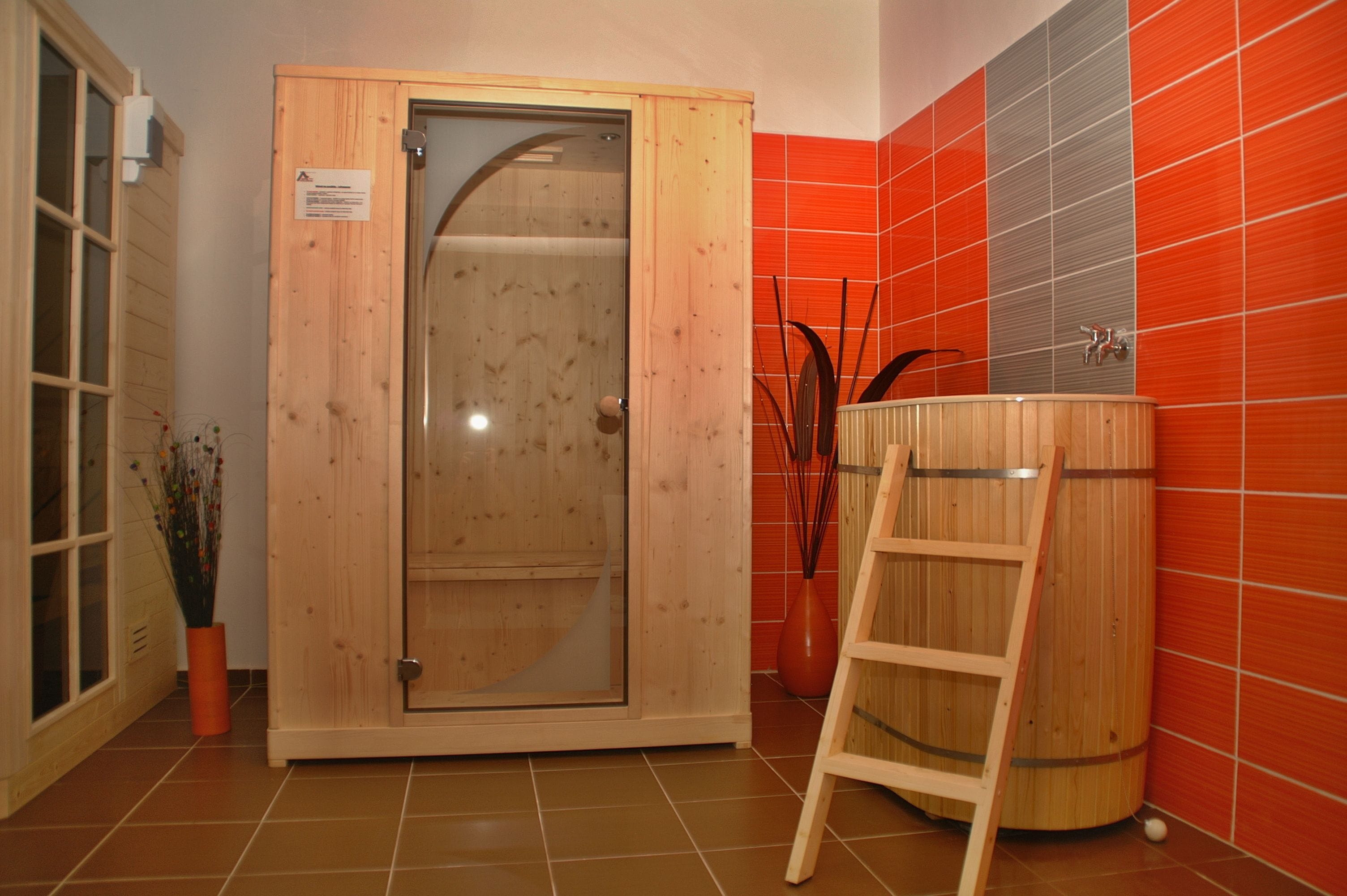 Ein Saunaraum mit Holztür, einer Holzleiter und einer roten Kachelwand.