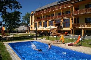 A swimming pool with a person swimming, surrounded by lounge chairs and umbrellas. - Hotel Avalanche (Stola)