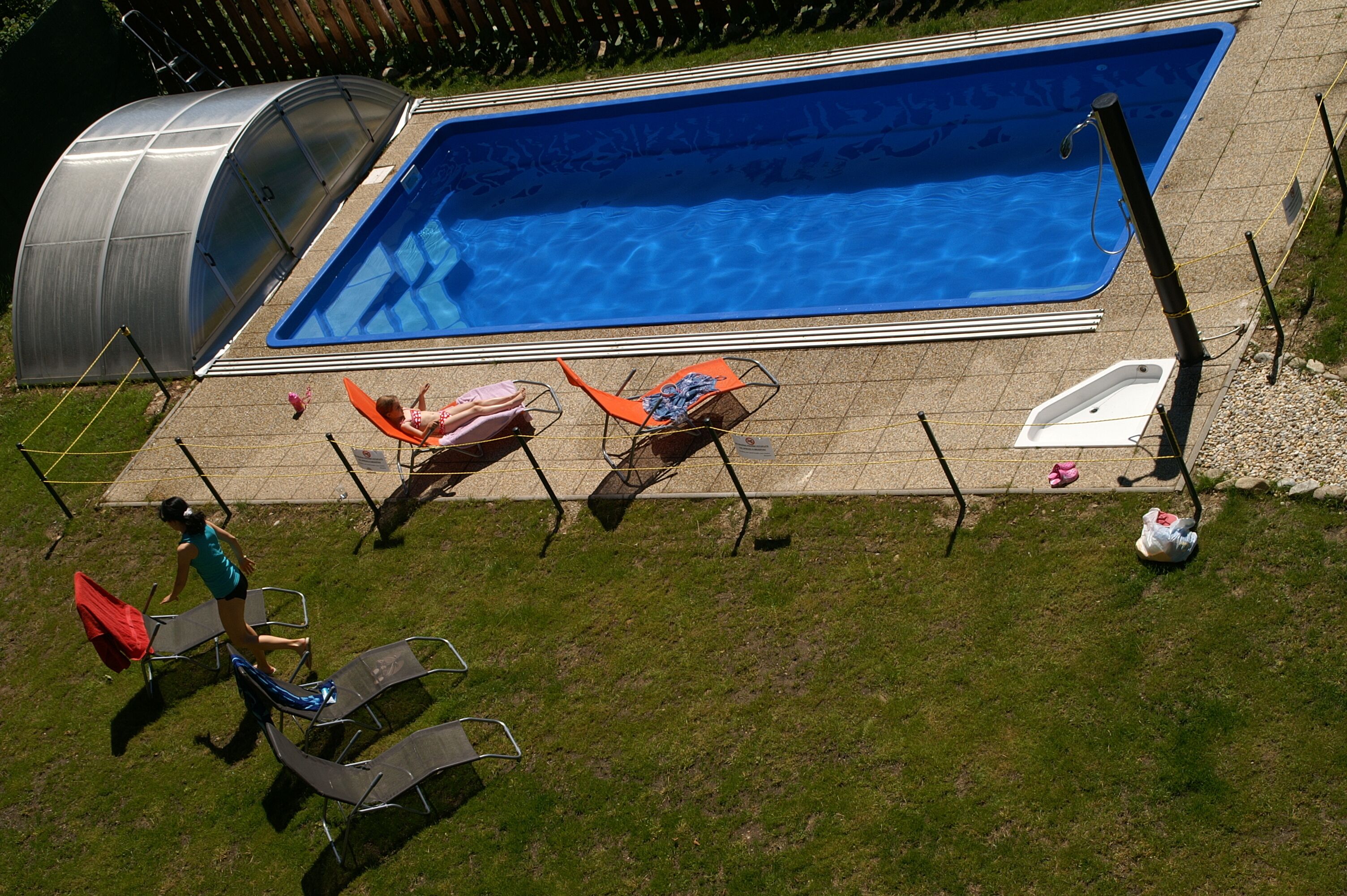 Ein Schwimmbecken mit Metallkonstruktion an einer Seite, Liegestühlen und einer kleinen Whirlwanne.