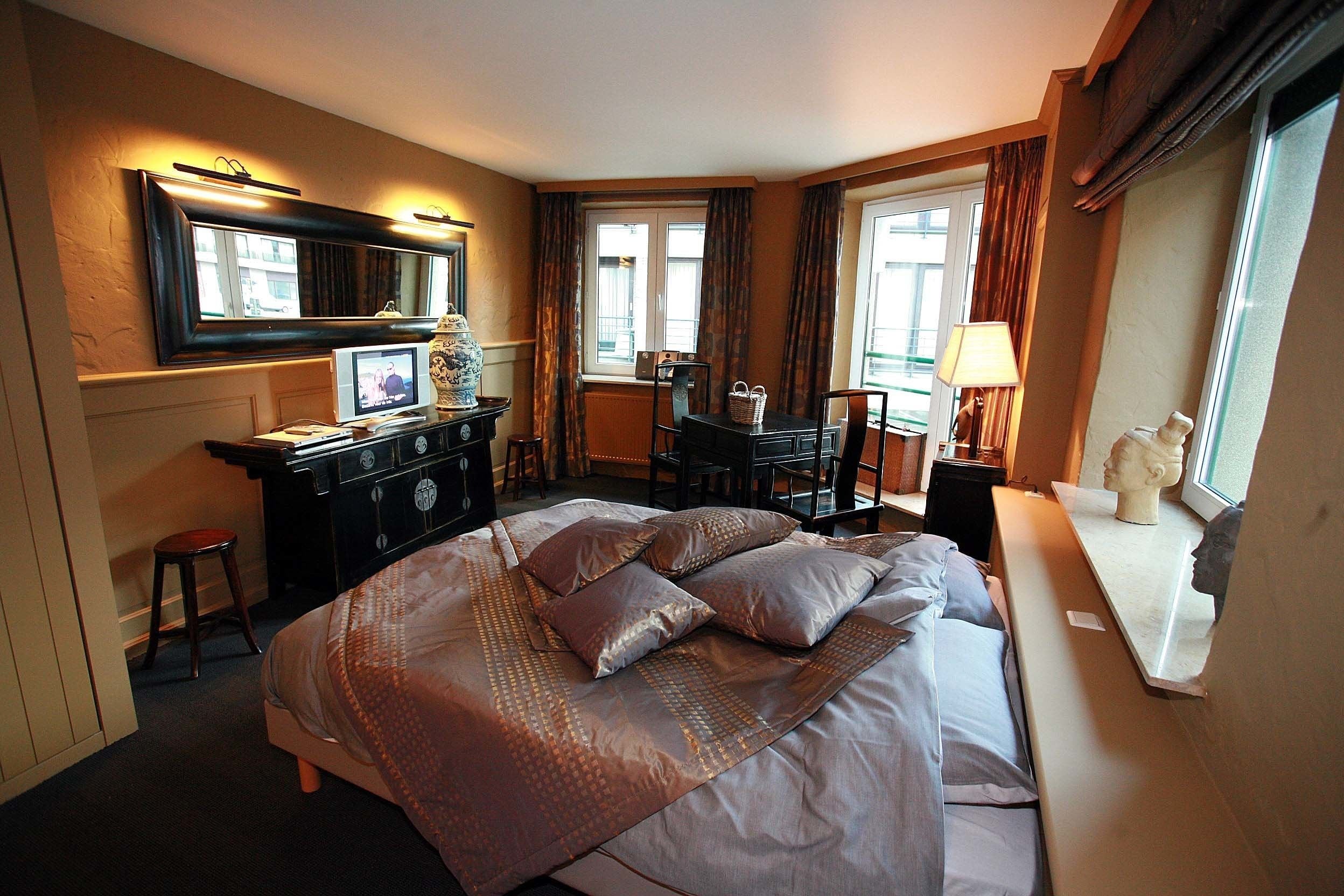 Habitación de hotel con una cama grande, un escritorio, una silla, un aparador y una ventana con cortinas.
