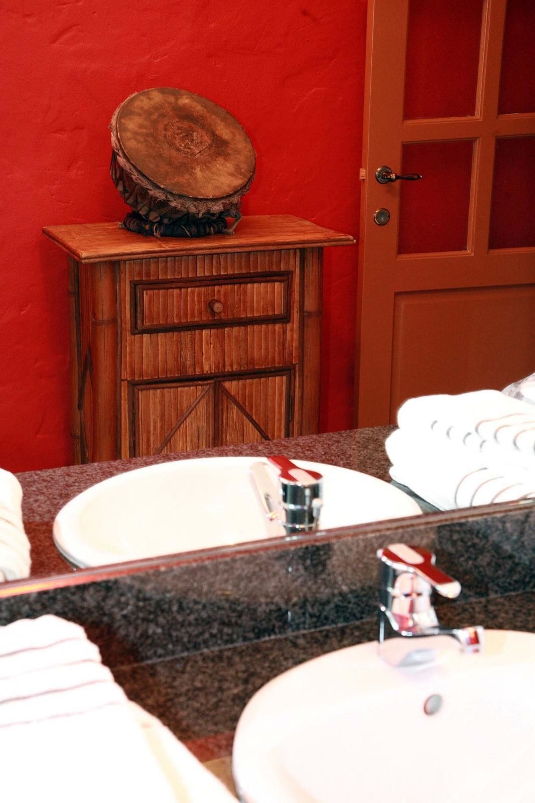Een badkamer met een houten wastafelmeubel, een rode muur en een deur.