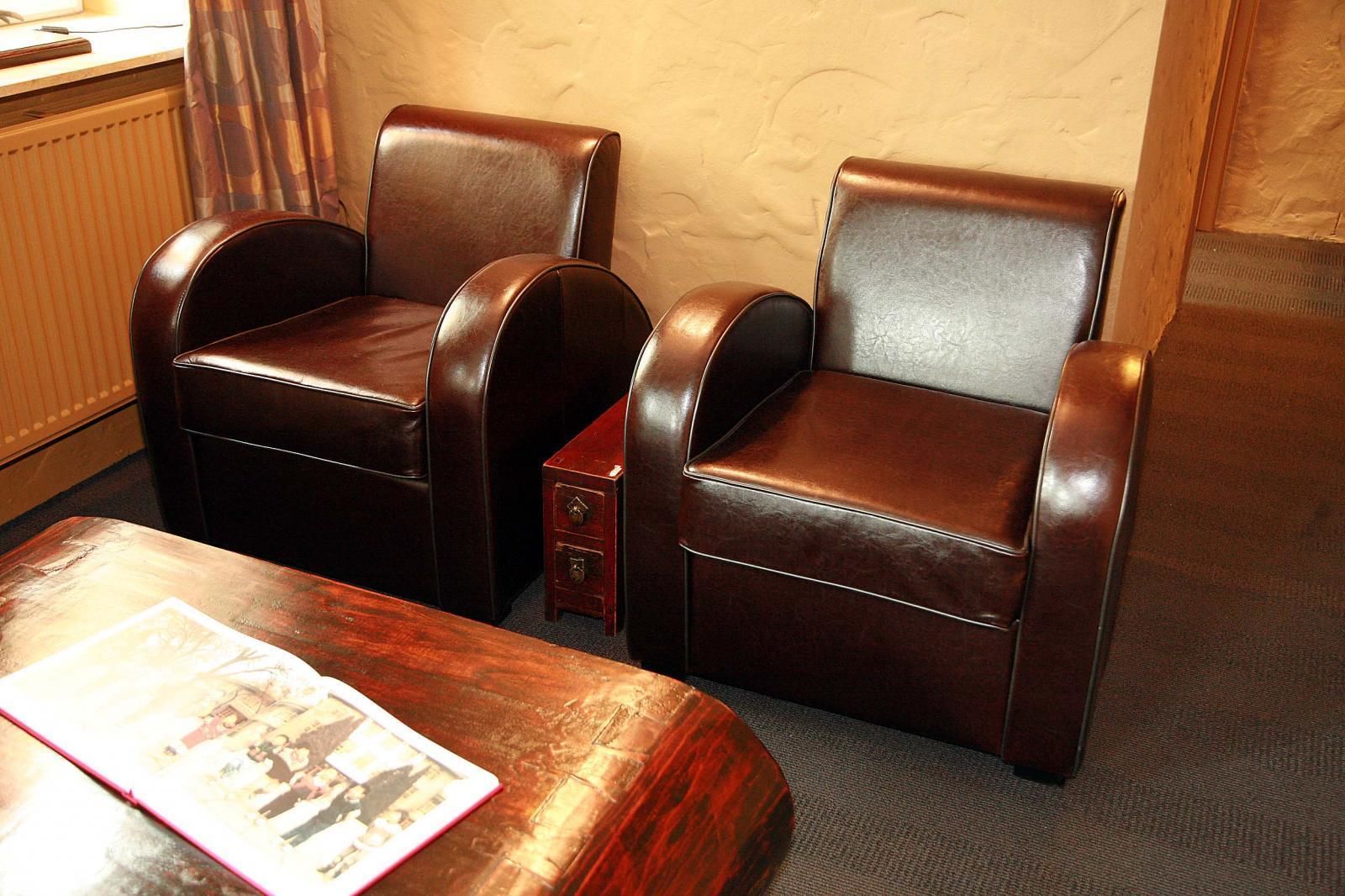A room with two leather armchairs, a small wooden side table, and a magazine on the table.