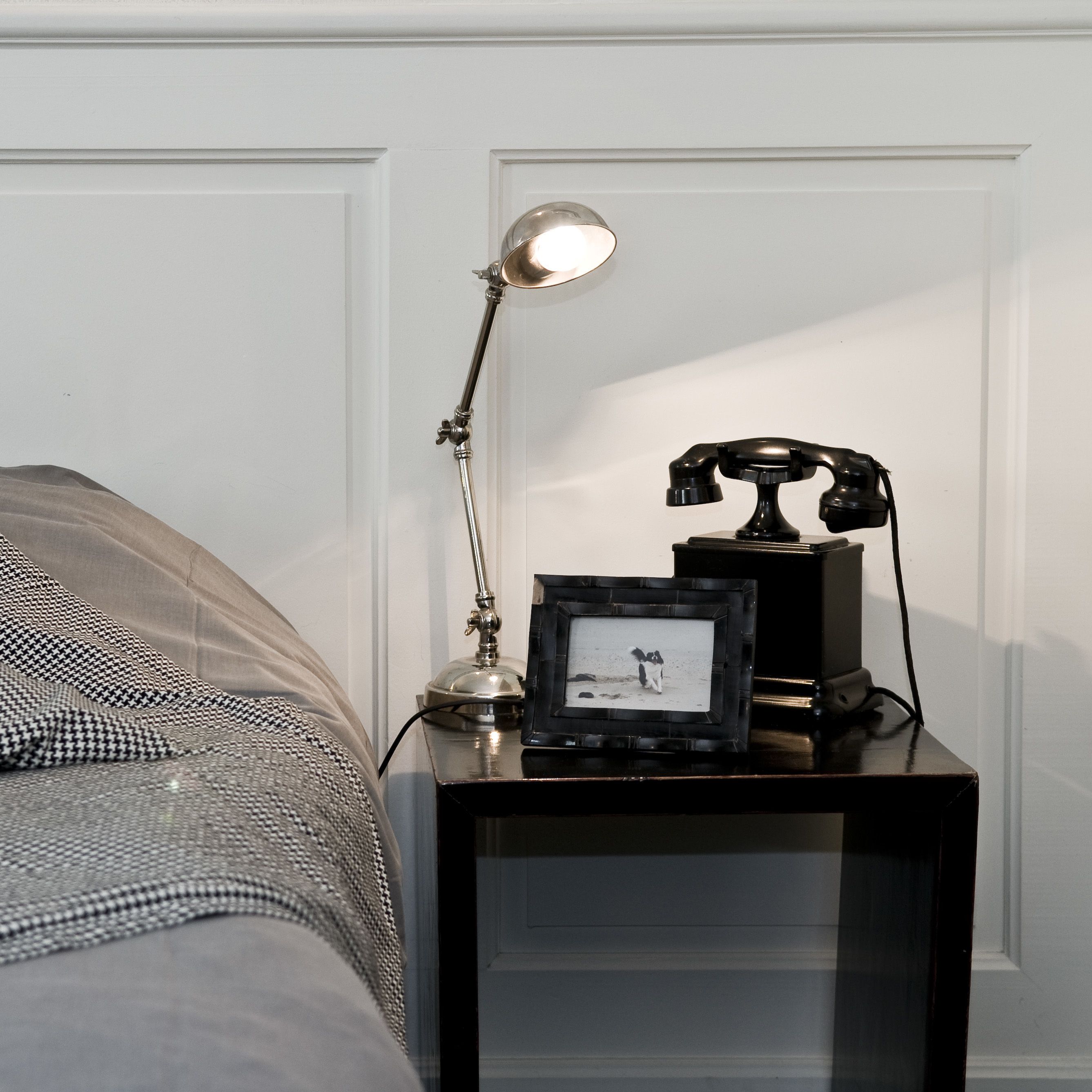 Een nachtkastje met een lamp, een telefoon en een ingelijste foto.