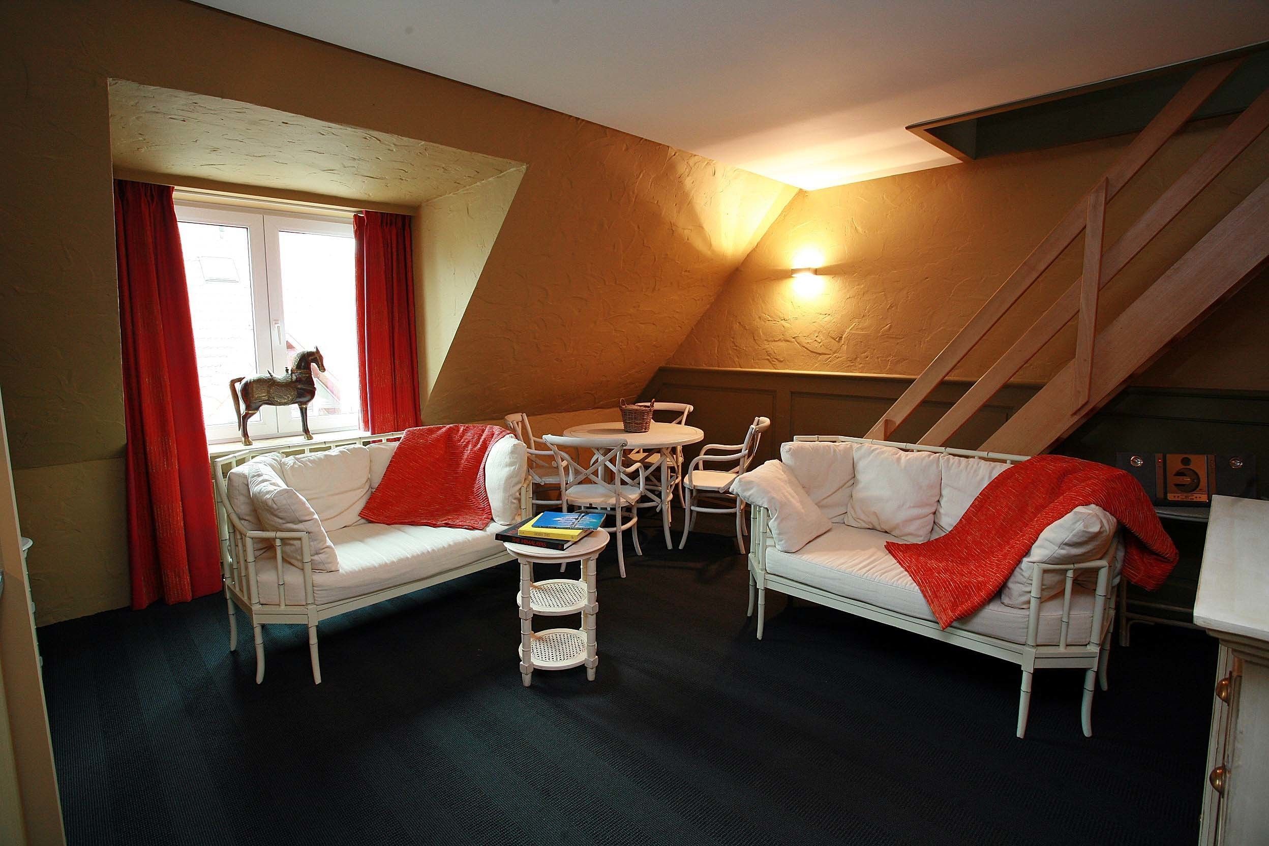 Una habitación acogedora con dos sofás blancos, una mesita redonda y una ventana con cortinas rojas.