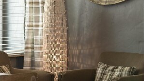 A cozy room with a plaid sofa, a tall woven floor lamp, and a round mirror on the wall. - De Laurier (Knokke-Heist)