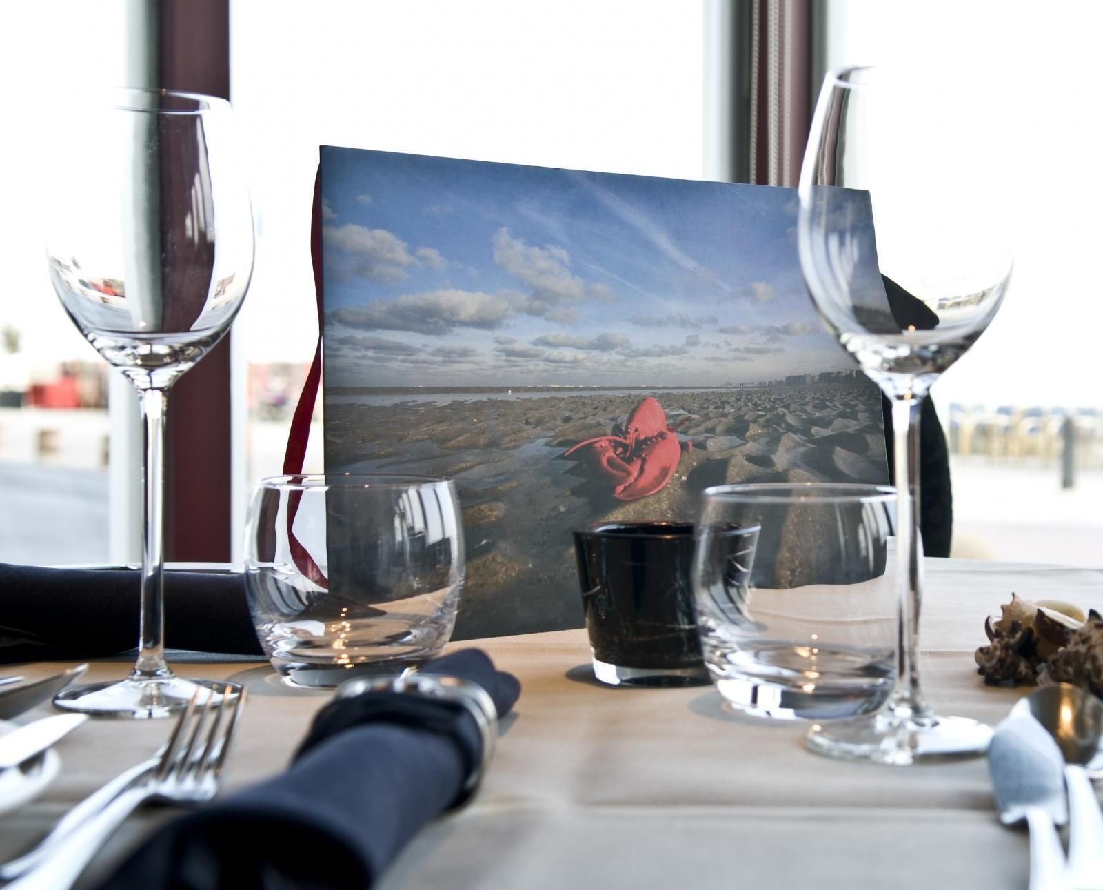 Una mesa dispuesta para comer, con una fotografía panorámica, vasos transparentes y una servilleta.