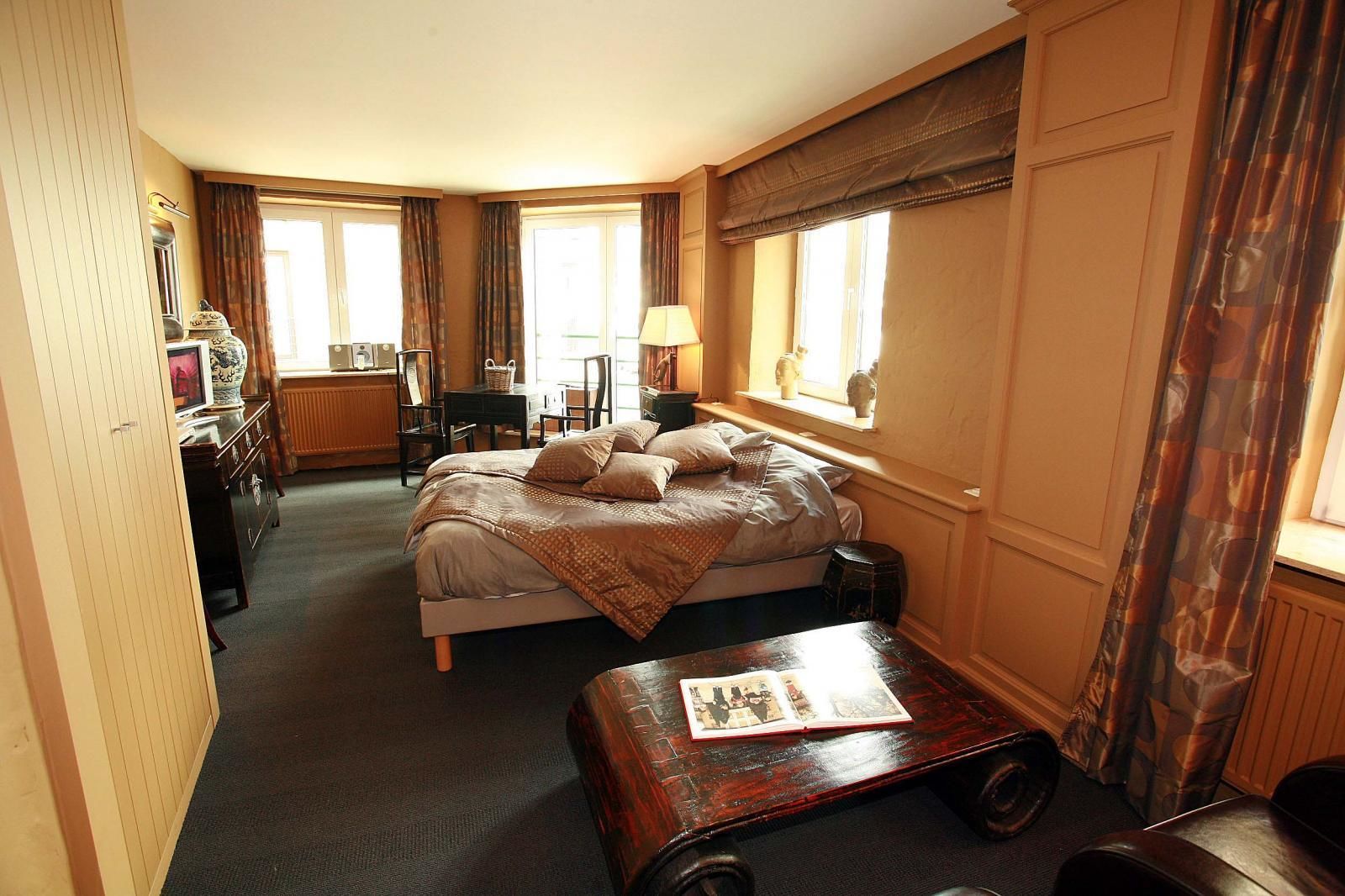 A hotel room with a bed, a desk, a chair, a lamp, and a window with curtains.