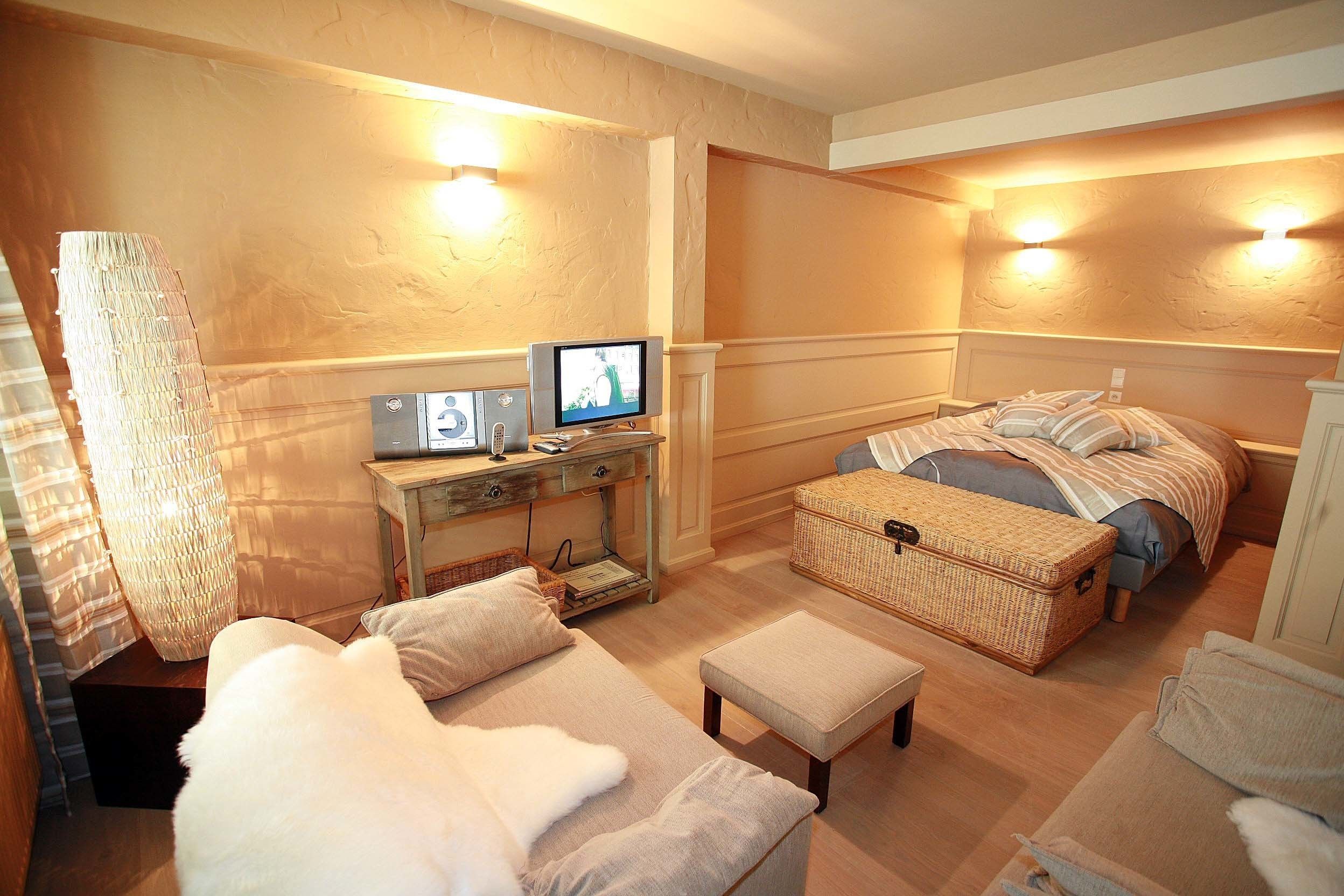 A cozy hotel room with a bed, a sofa, a small table with a television, and a wicker chest.