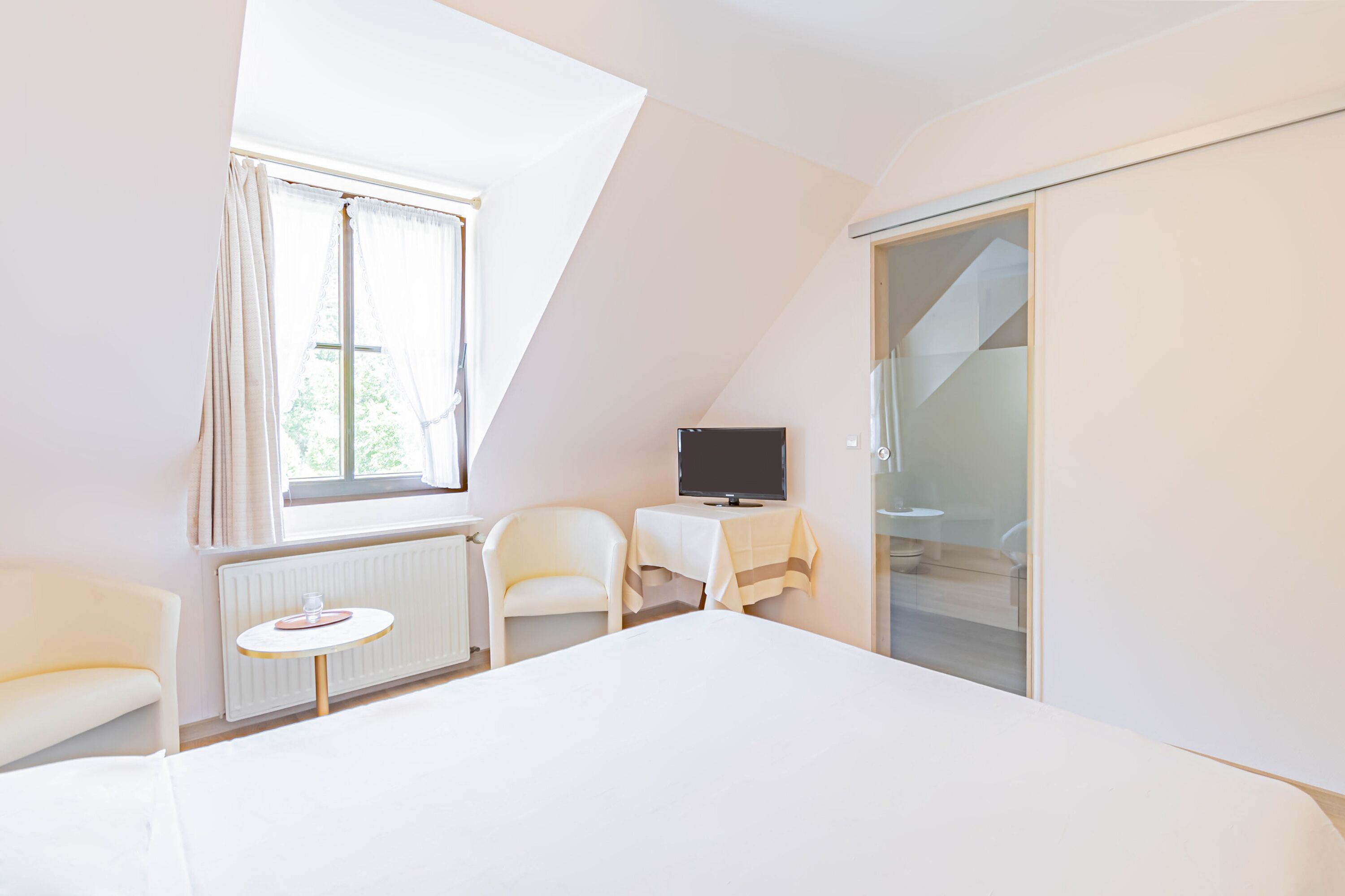Una habitación de hotel moderna con una cama grande, un televisor sobre una mesita, una silla y un armario con puerta corredera de vidrio.