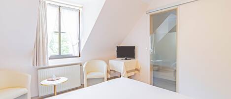 Una habitación de hotel moderna con una cama grande, un televisor sobre una mesita, una silla y un armario con puerta corredera de vidrio.