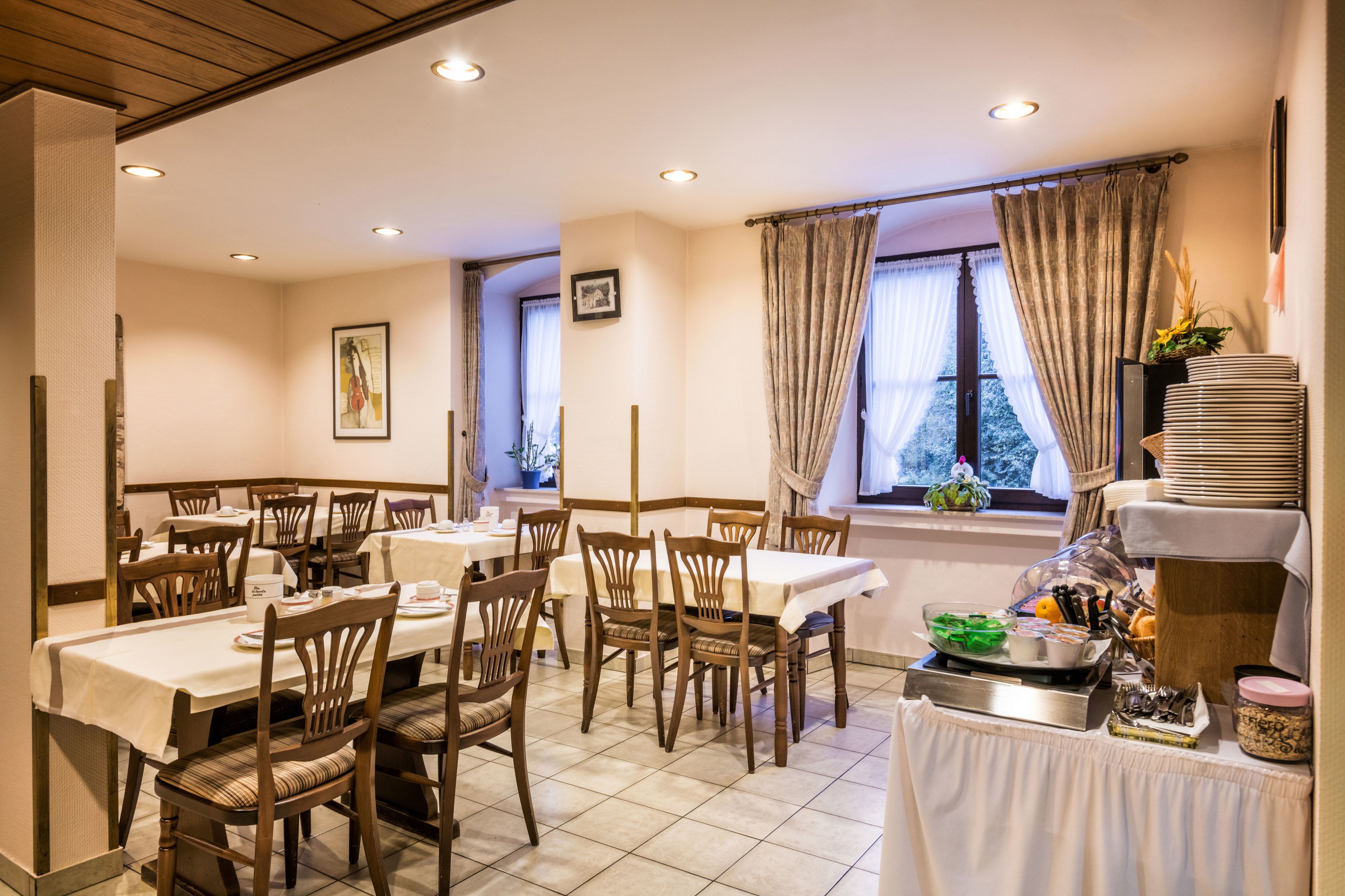 Un espace repas avec plusieurs tables et chaises, un buffet proposant divers plats, et une fenêtre avec des rideaux.