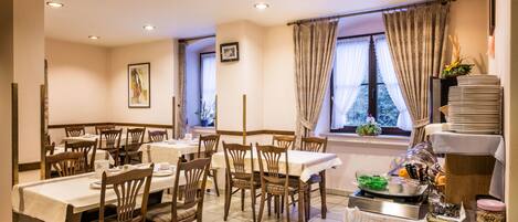 A dining area with multiple tables and chairs, a buffet station with food items, and a window with curtains.