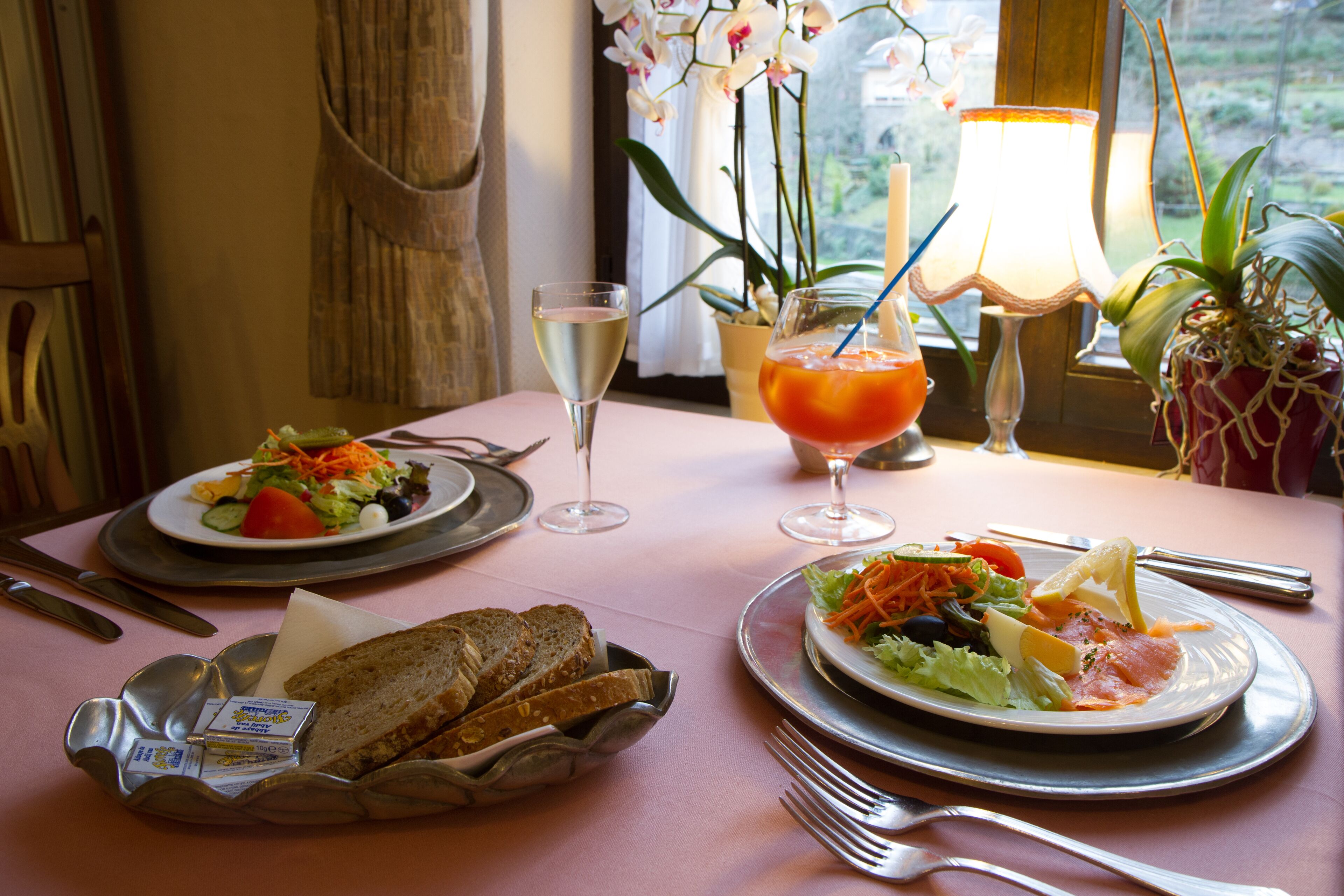 A dining table with plates of food, a basket of bread, and a glass of wine.