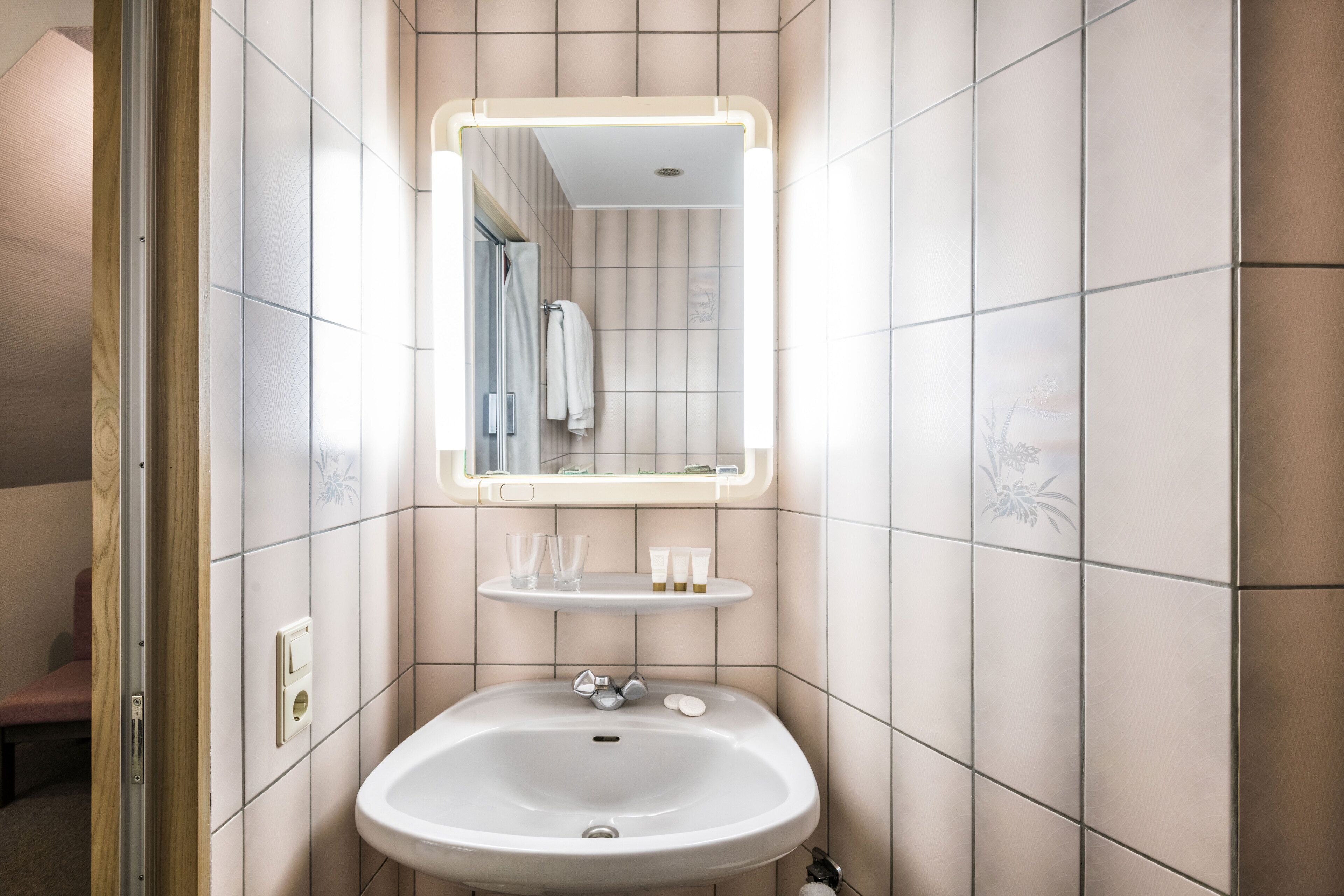 A bathroom with a white sink, a mirror with a light, and a shelf with toiletries.