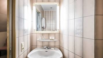 A bathroom with a white sink, a mirror with a light, and a shelf with toiletries.