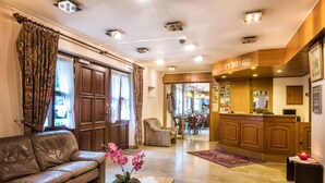 Un vestíbulo de hotel con mostrador de recepción, sofá de cuero y una orquídea en maceta.