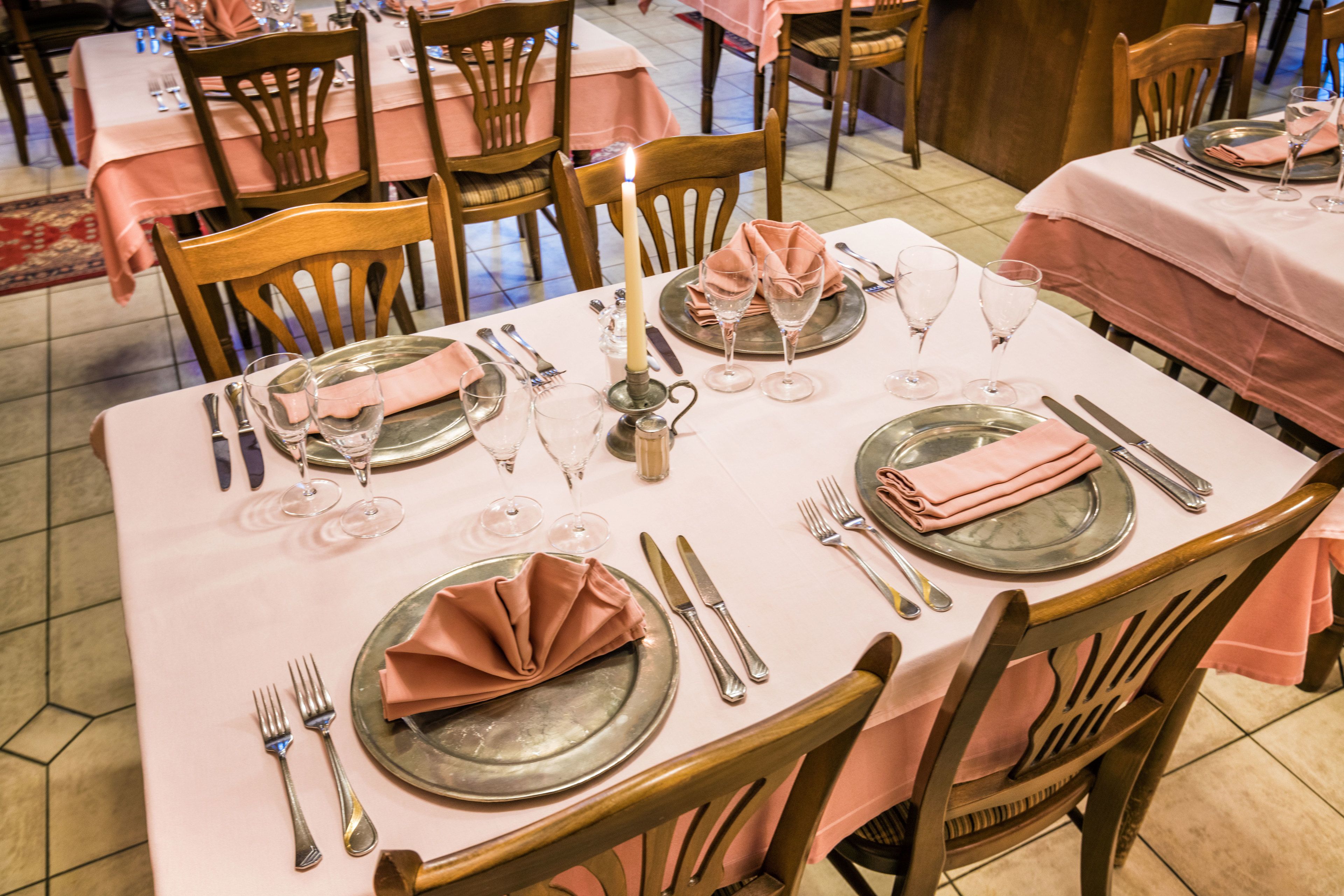A dining table set with pink tablecloths, wooden chairs, and silverware.