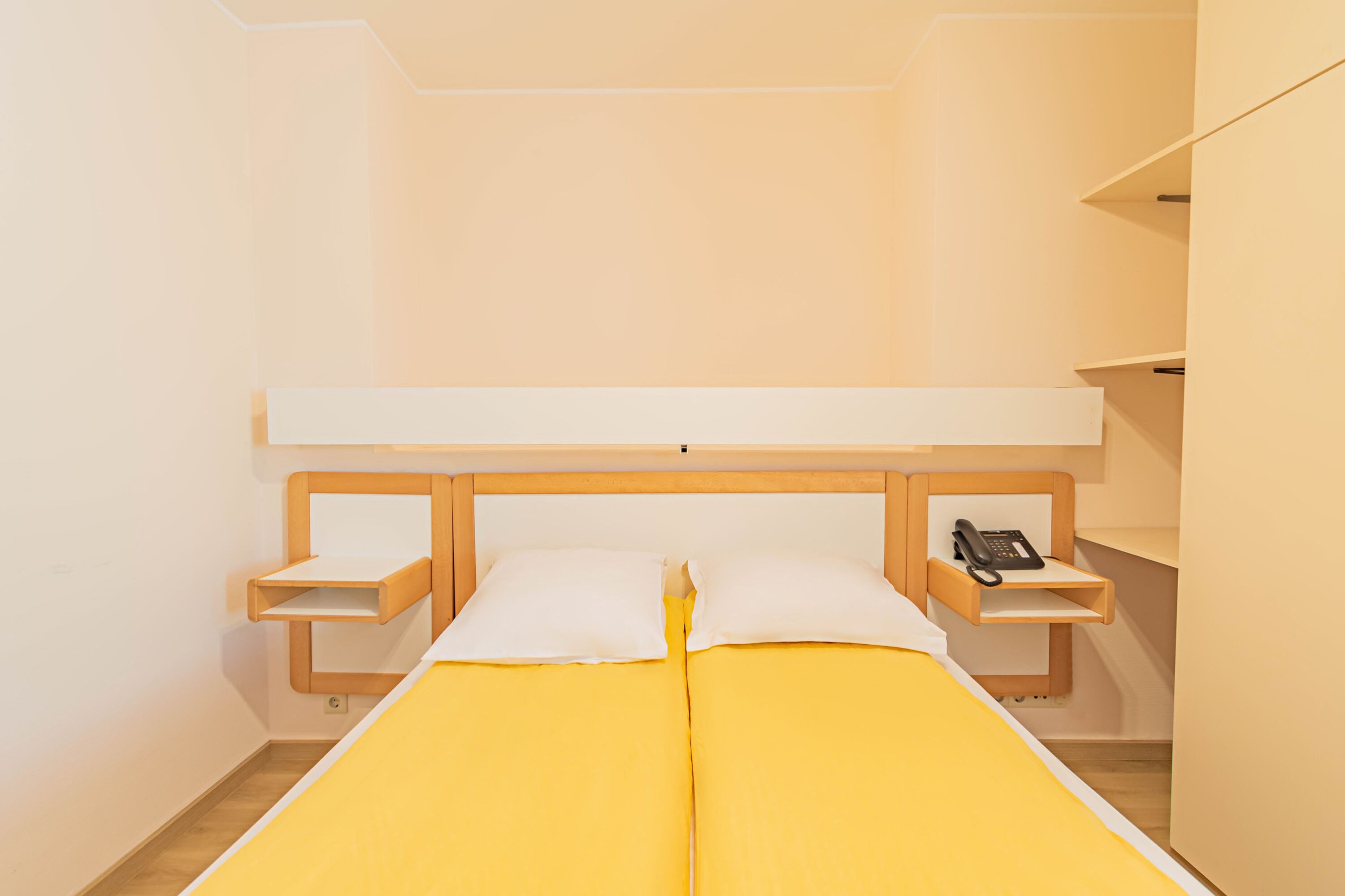 A single bed with a wooden headboard, two bedside tables, and a phone on one of the tables.