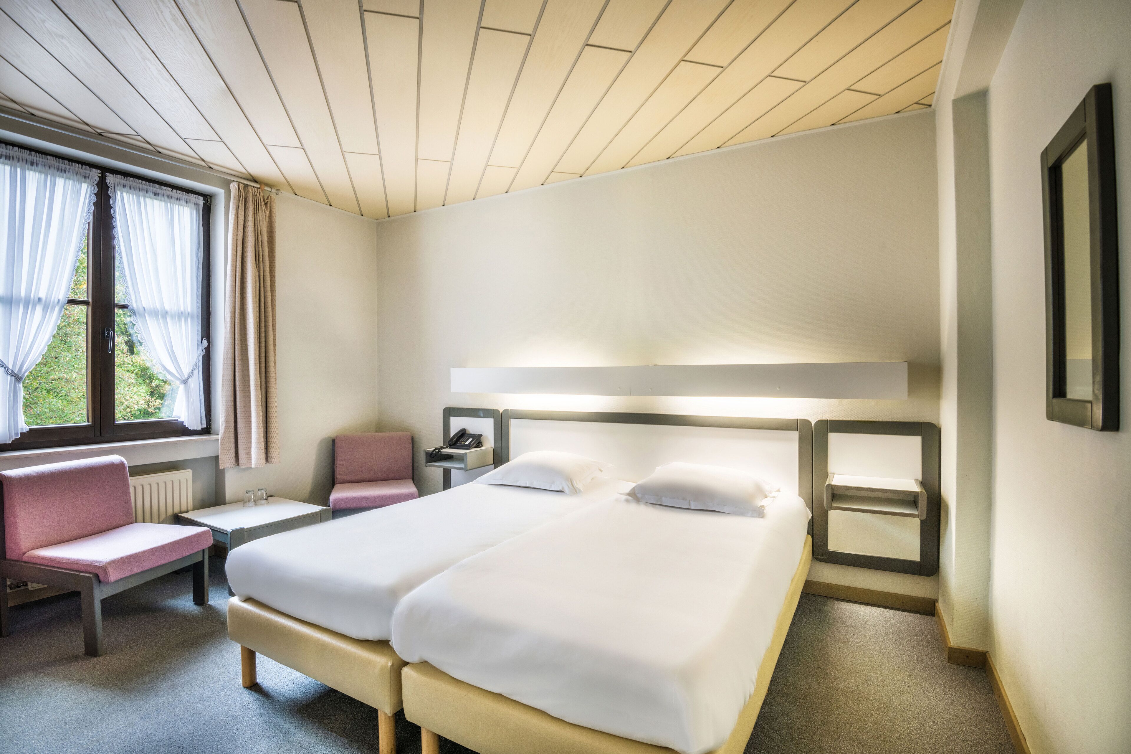 A hotel room with two beds, a desk, a chair, and a window with curtains.