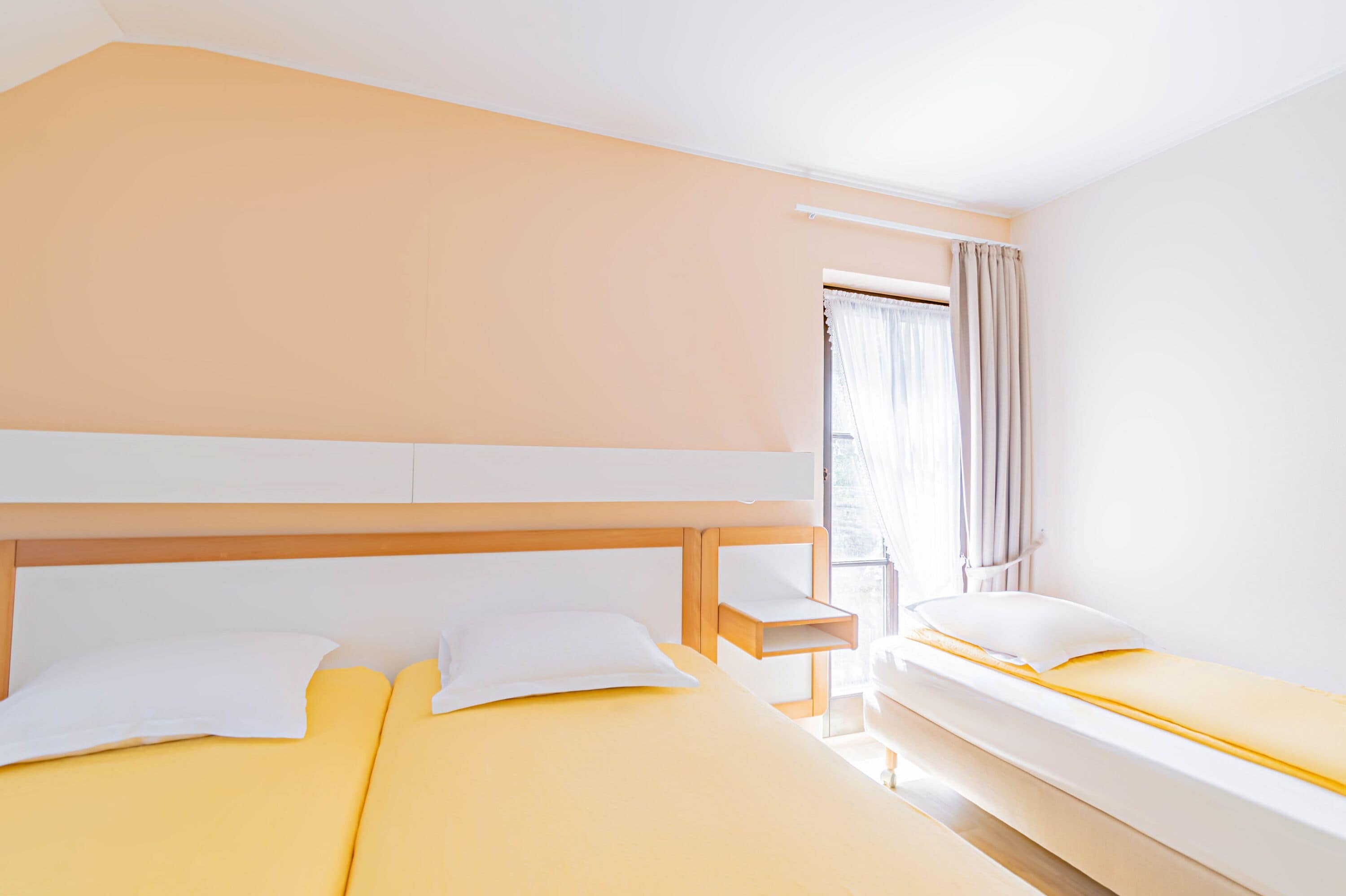 Hotellihuone, jossa on kaksi sänkyä, puinen pääty ja ikkuna, jossa on verhot.